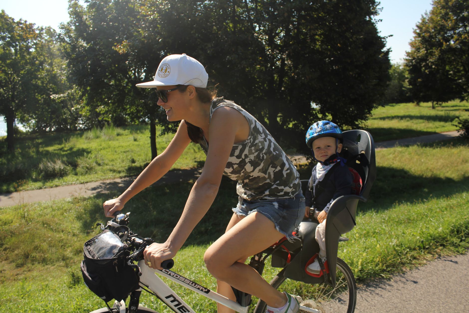 Kvinna cyklar med ett litet barn med hjälm i bakmonterad barnsits
