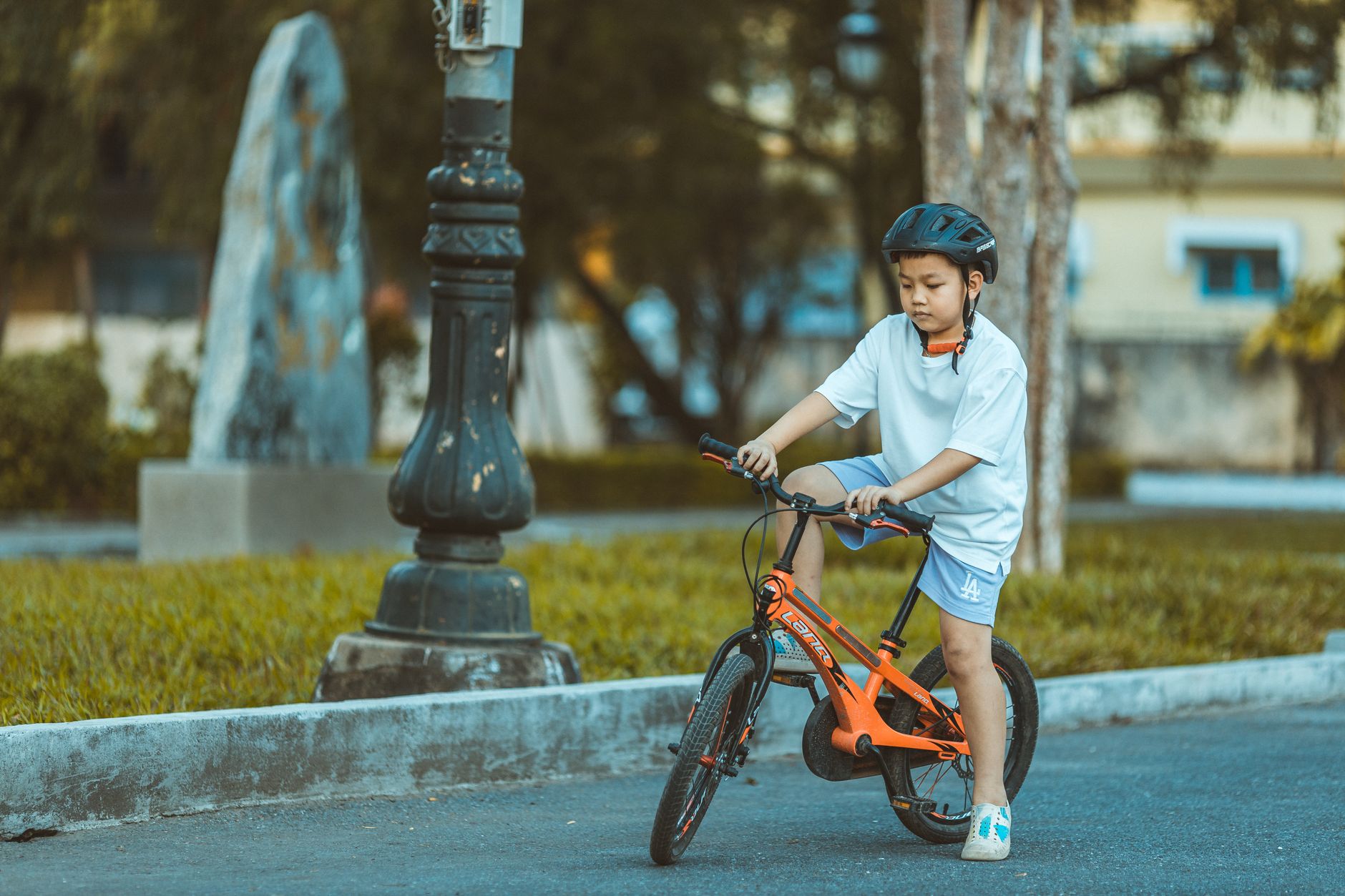 Pojke med cykelhjälm på en orange barncykel på en asfalterad parkväg