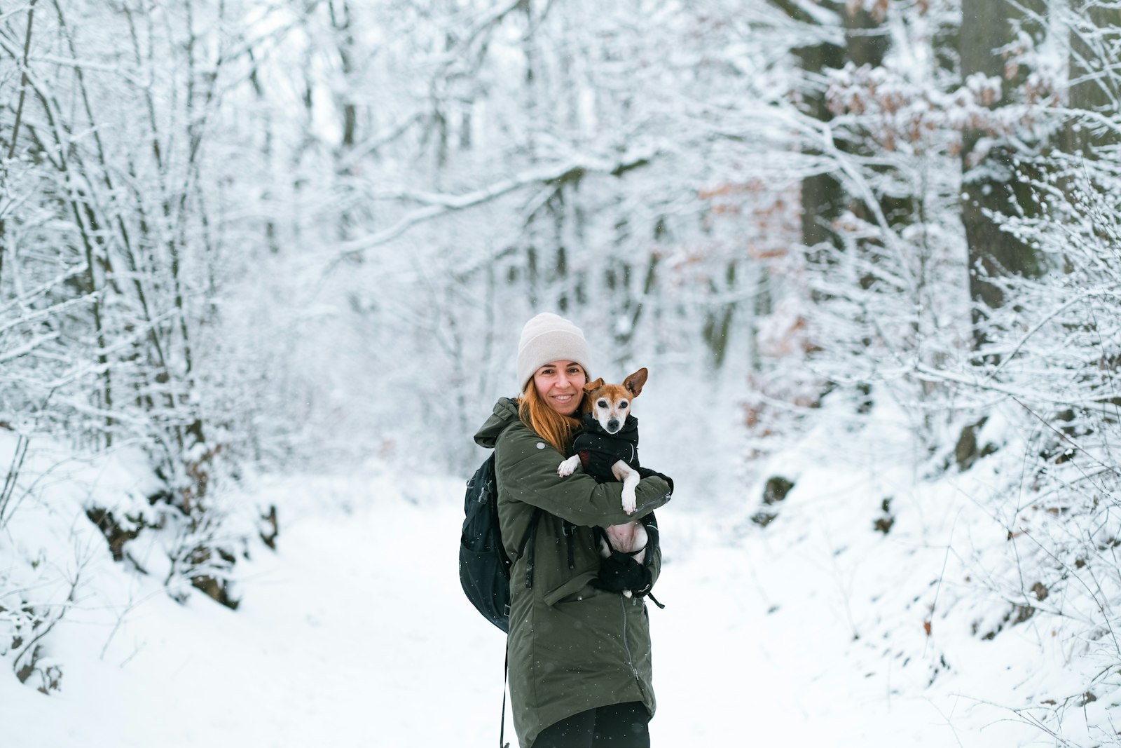 Kvinna håller en liten hund i famnen på en snöig skogsstig