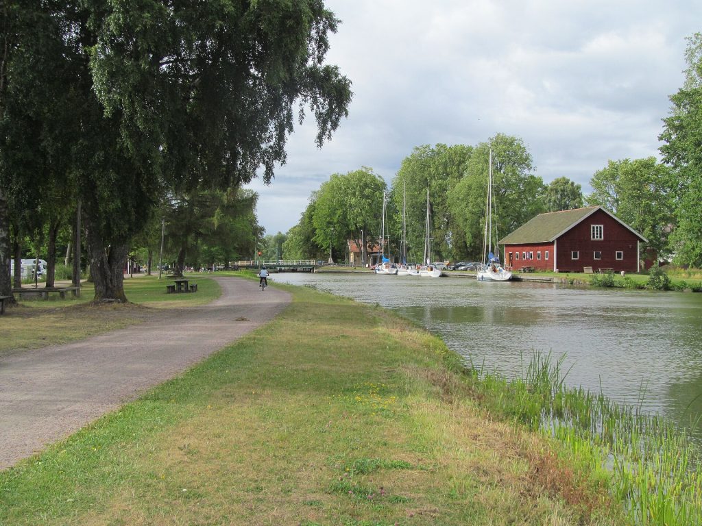 Dragvägen längs Göta kanal vid Hajstorp med förtöjda segelbåtar och ett rött kanalmagasin