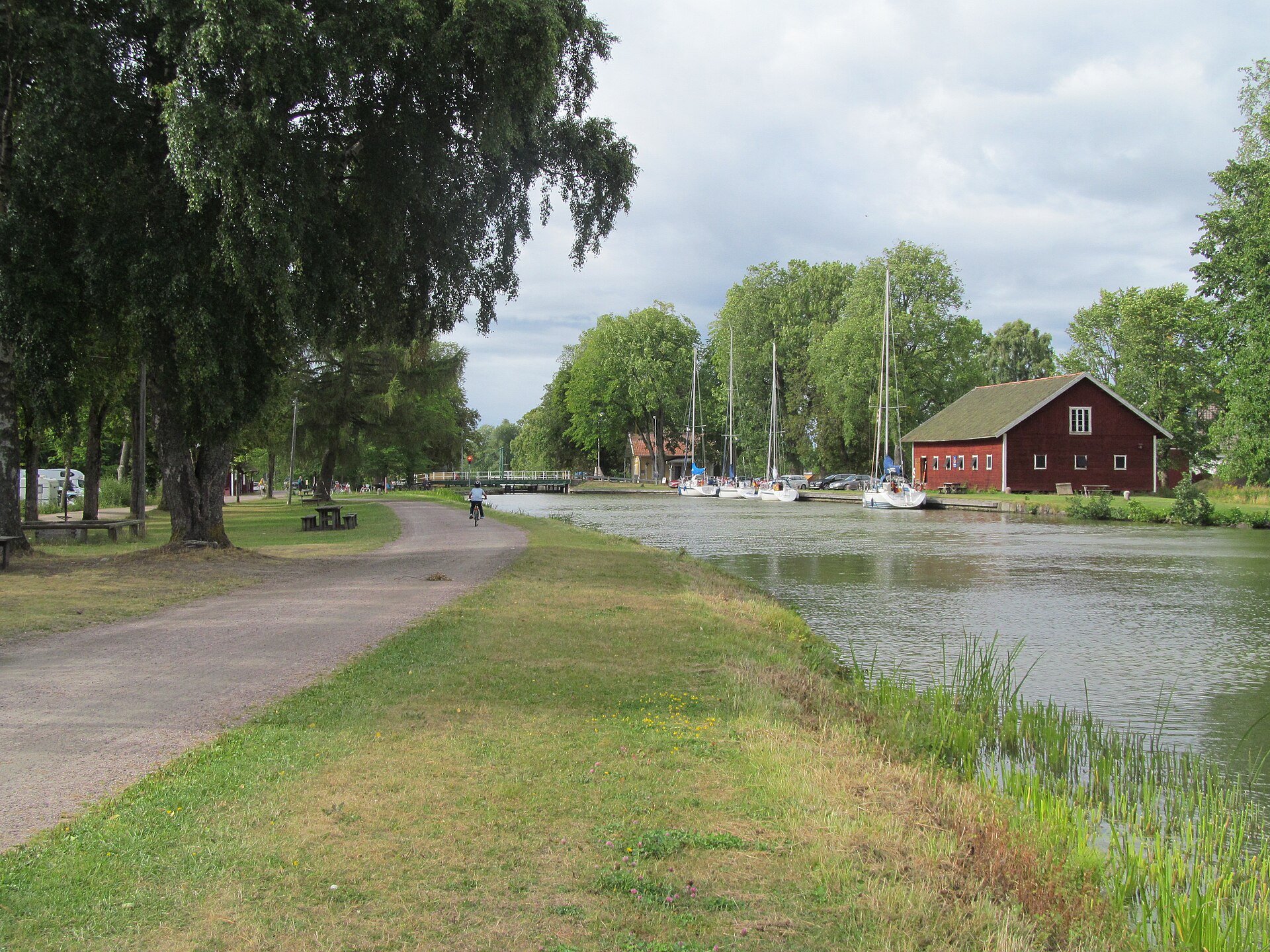 Dragvägen längs Göta kanal vid Hajstorp med förtöjda segelbåtar och ett rött kanalmagasin