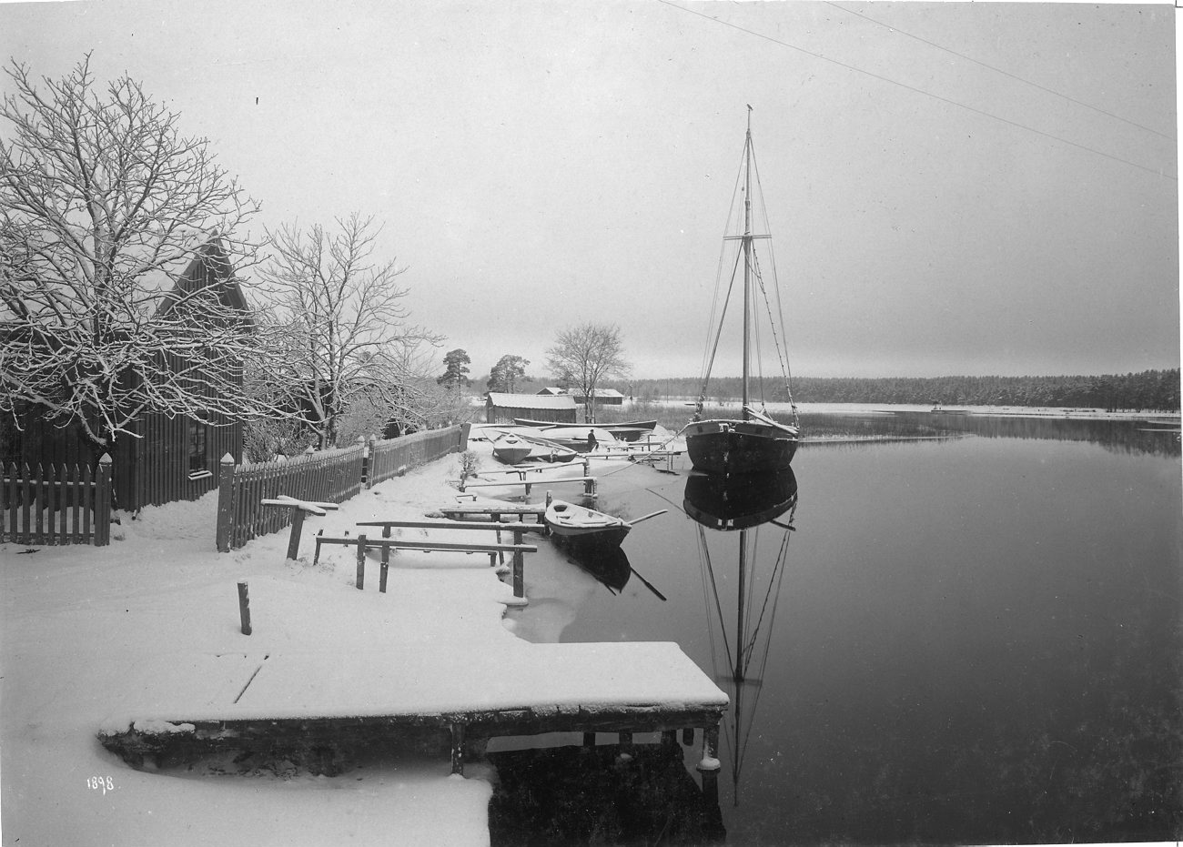 Snötäckt brygga och förtöjda båtar vid Rödesund i Göta kanal en vinterdag 1898