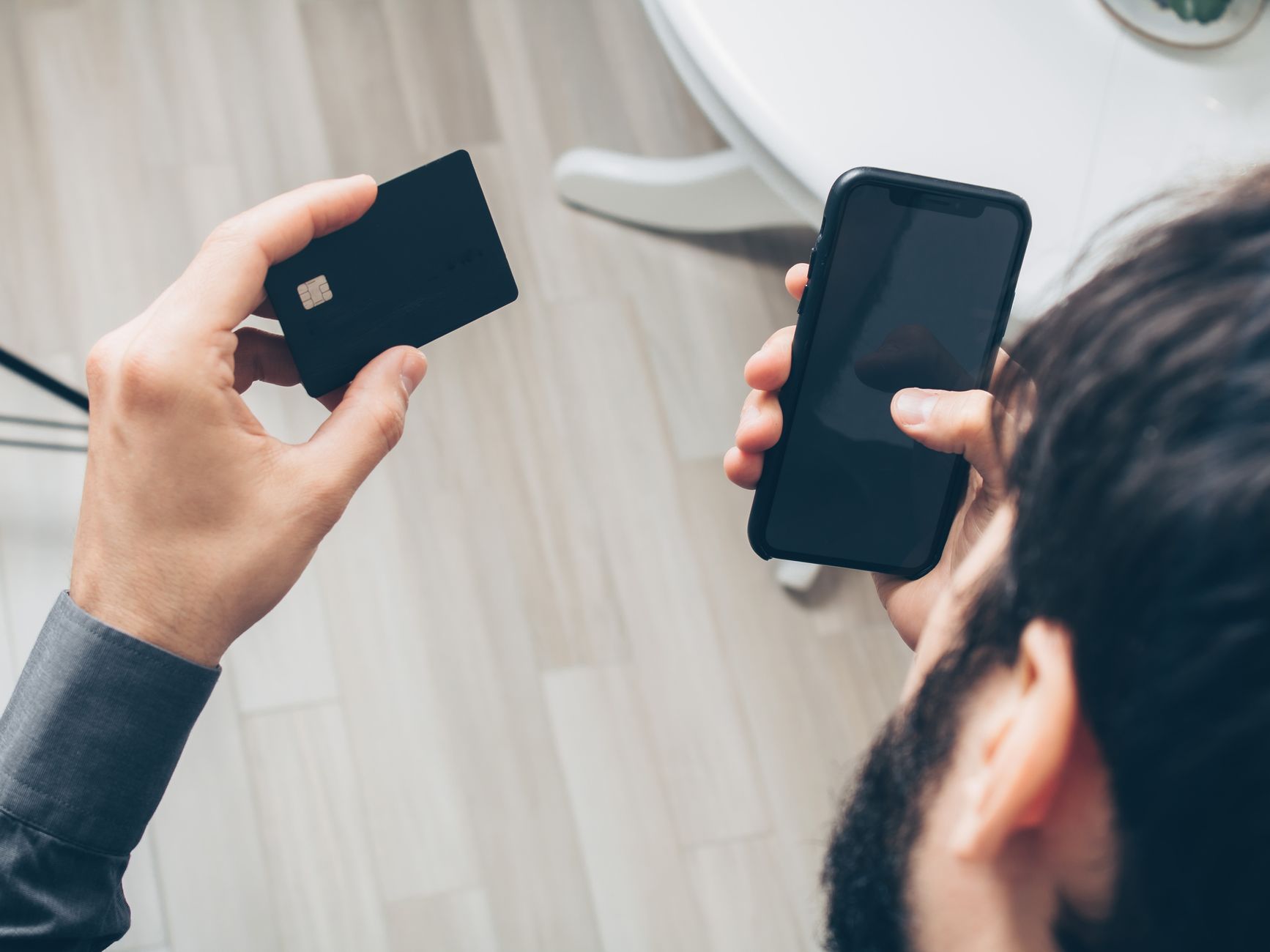 Man som håller ett bankkort och en mobiltelefon