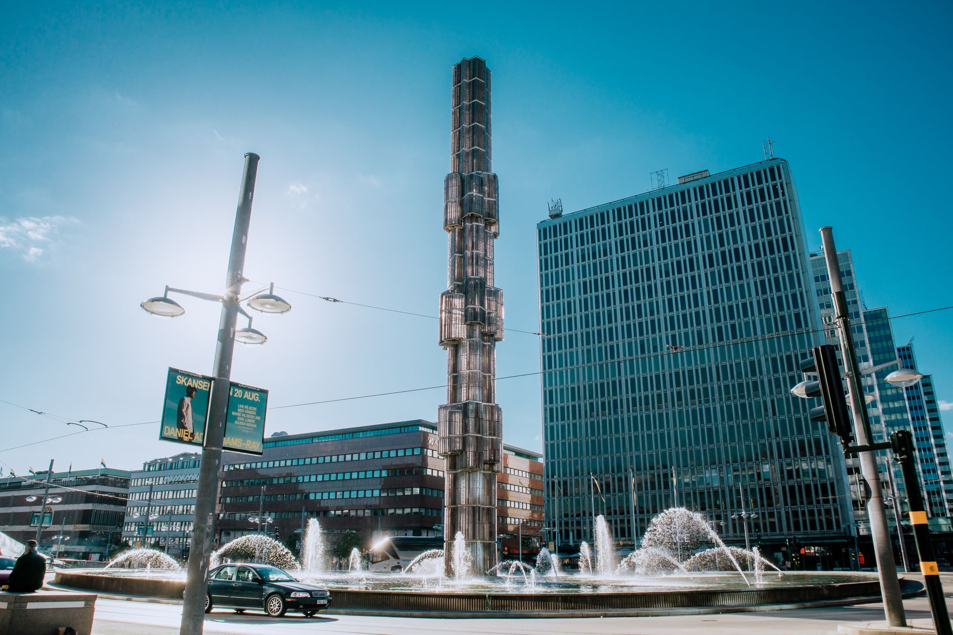 Kontorsbyggnader kring Sergels torg i centrala Stockholm en solig dag, med fontänen och glasobelisken i förgrunden