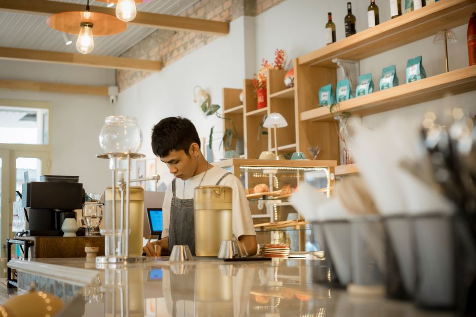 En ung barista arbetar bakom disken i ett kafé under ett sommarjobb