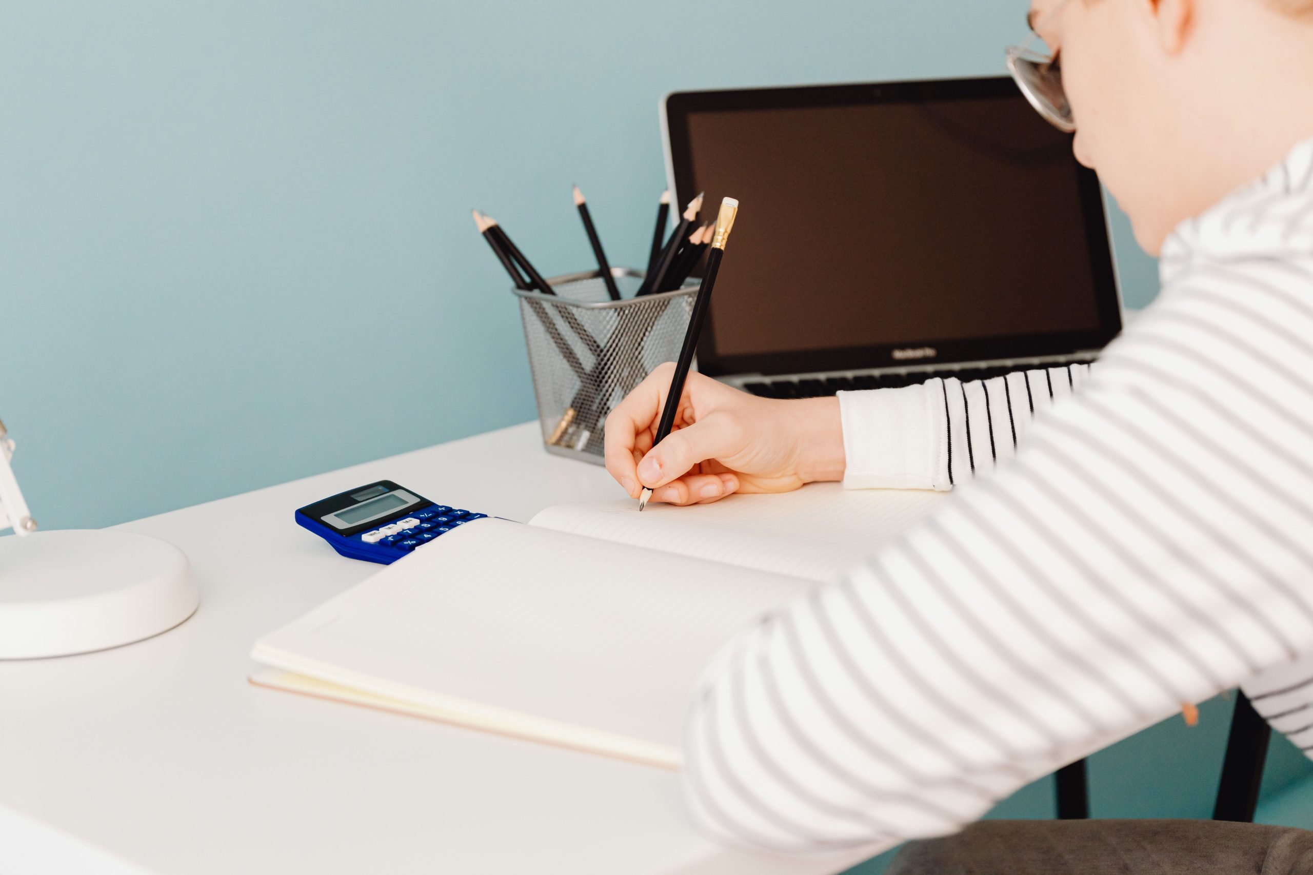 Ung student sitter vid ett ljust skrivbord med miniräknare, anteckningsblock och laptop