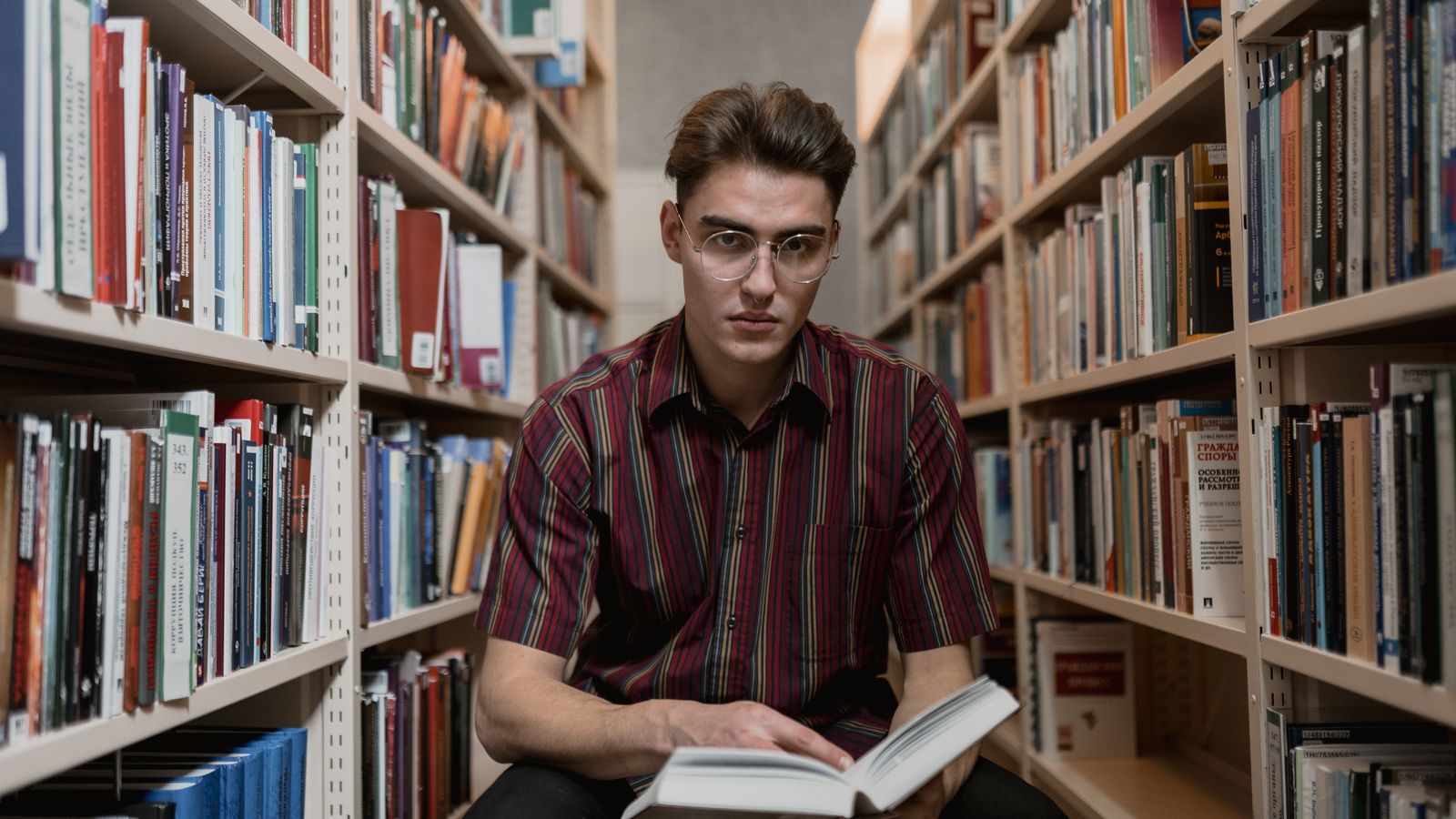 Ung man läser en bok mellan bokhyllor i ett bibliotek