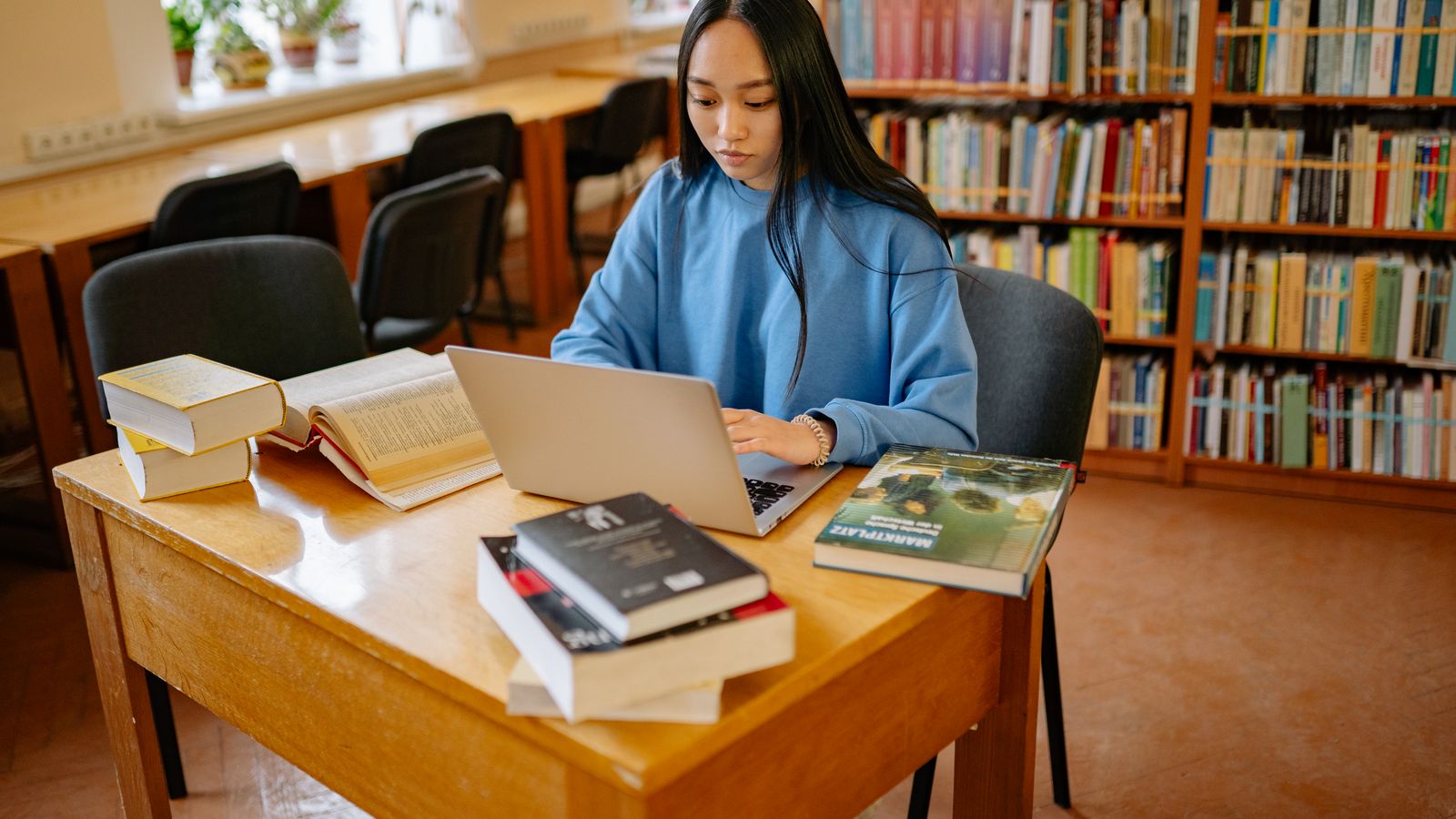Ung person studerar koncentrerat vid ett skrivbord med dator och böcker
