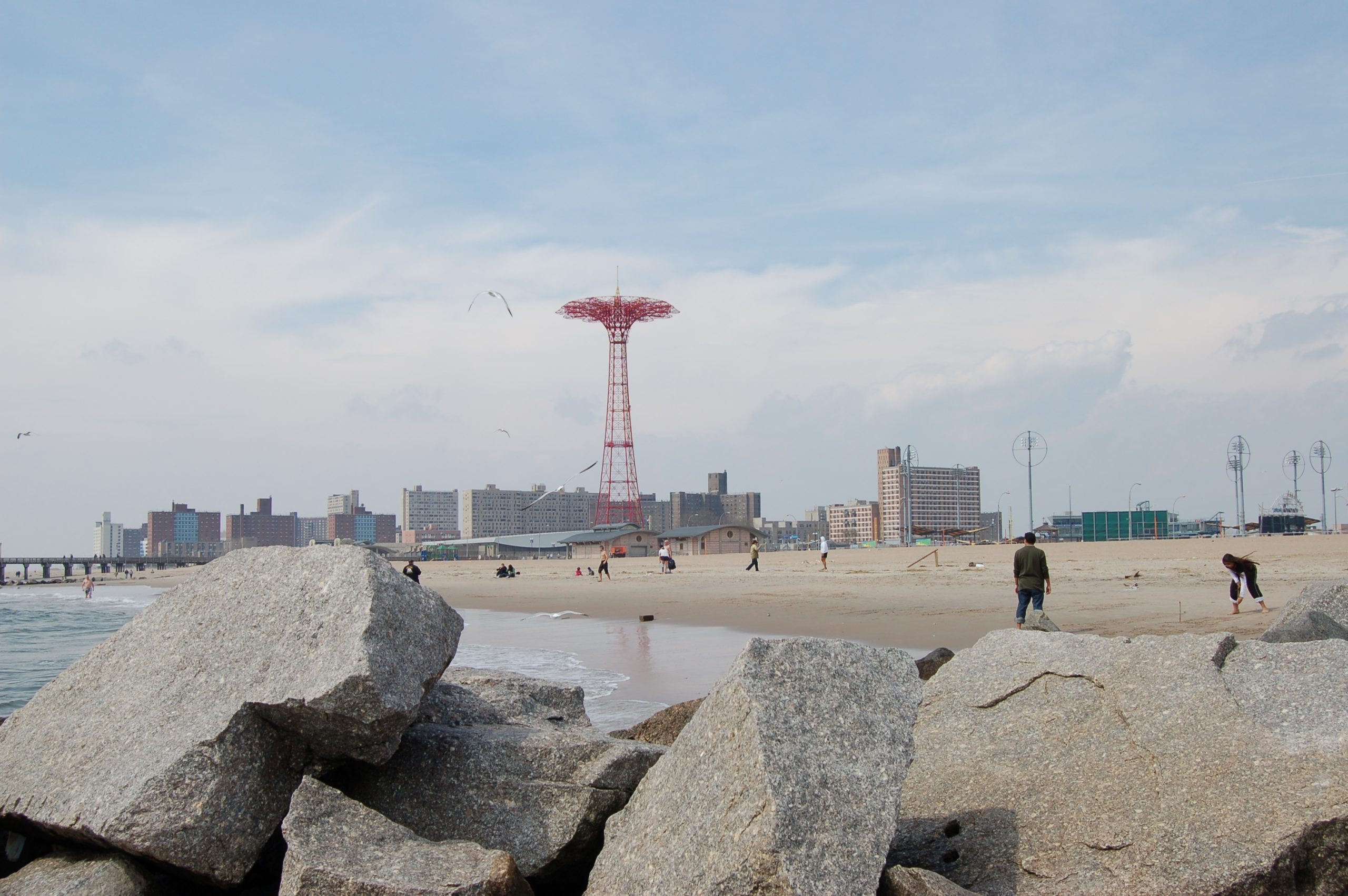 Stranden vid Brighton Beach i Brooklyn med en stenpir i förgrunden och fallskärmstornet Parachute Jump på Coney Island i bakgrunden