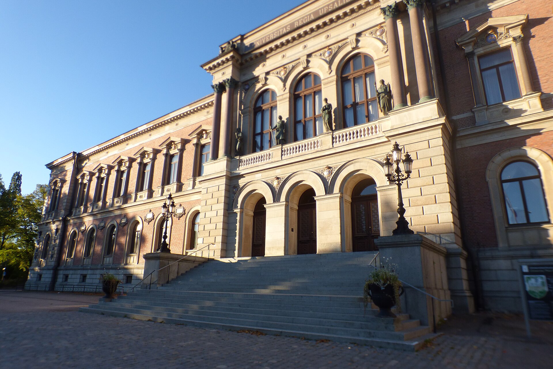 Universitetshuset i Uppsala med stentrappan och de tre rundbågade portarna i kvällssol