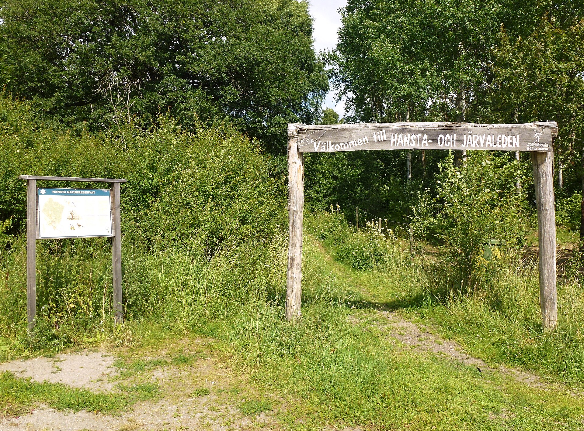 Träportal med texten Välkommen till Hansta- och Järvaleden, bredvid en informationstavla om Hansta naturreservat