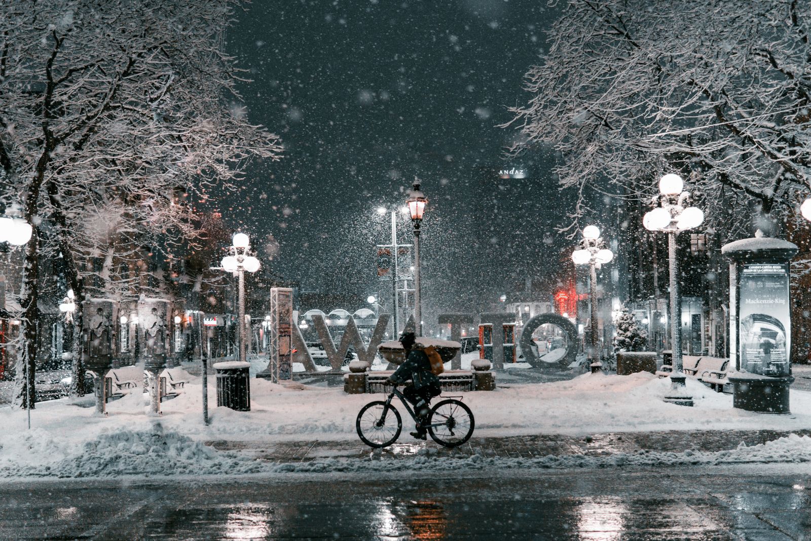 Cyklist på en snötäckt gata i tätt snöfall, upplyst av gatlyktor i vintermörker