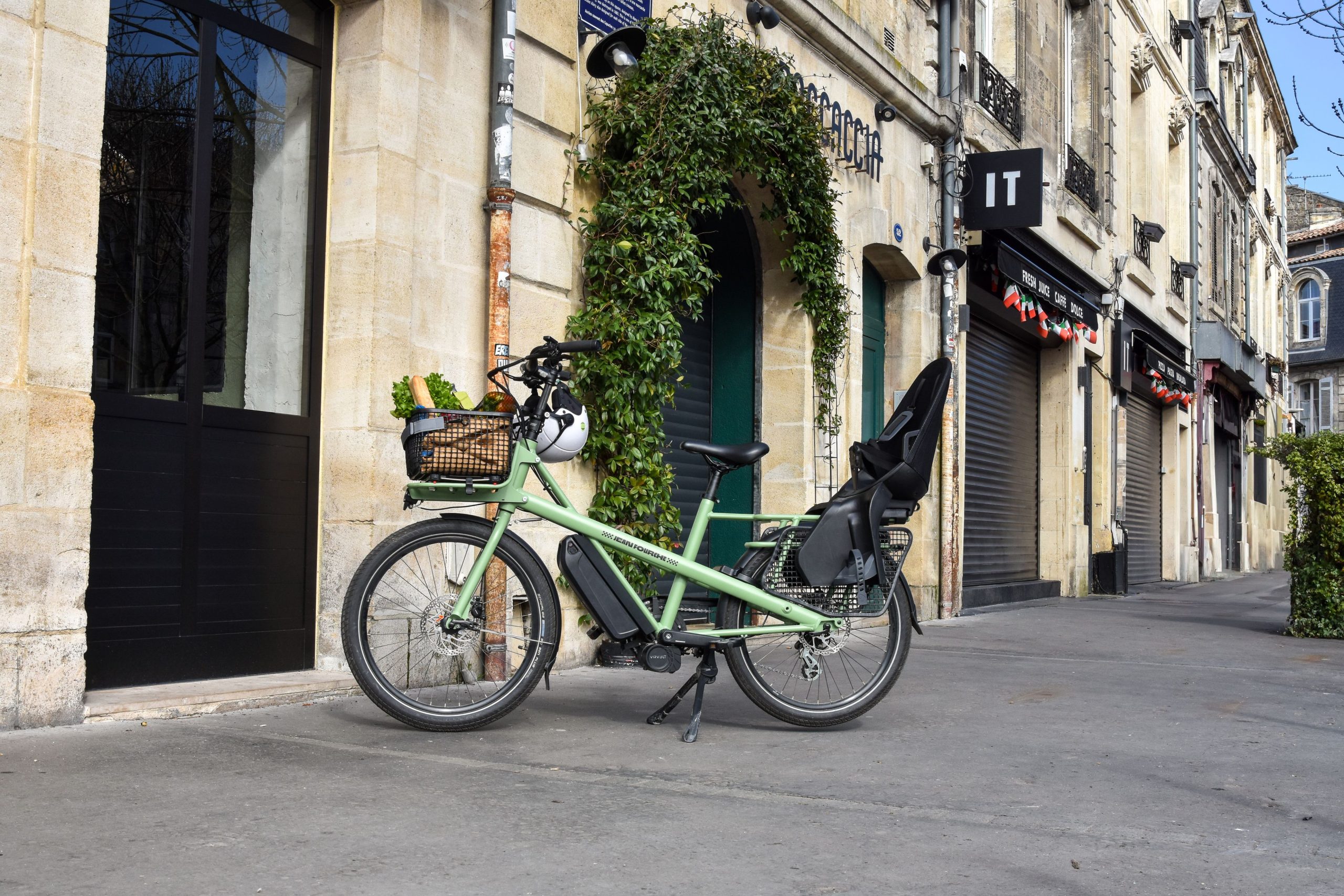 Grön lastcykel med monterad barnsits och packad korg