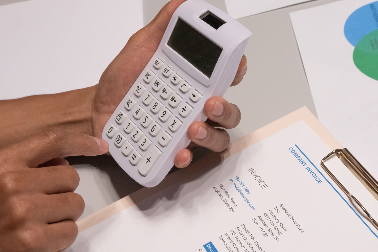 Hand med miniräknare och budgetunderlag på ett skrivbord