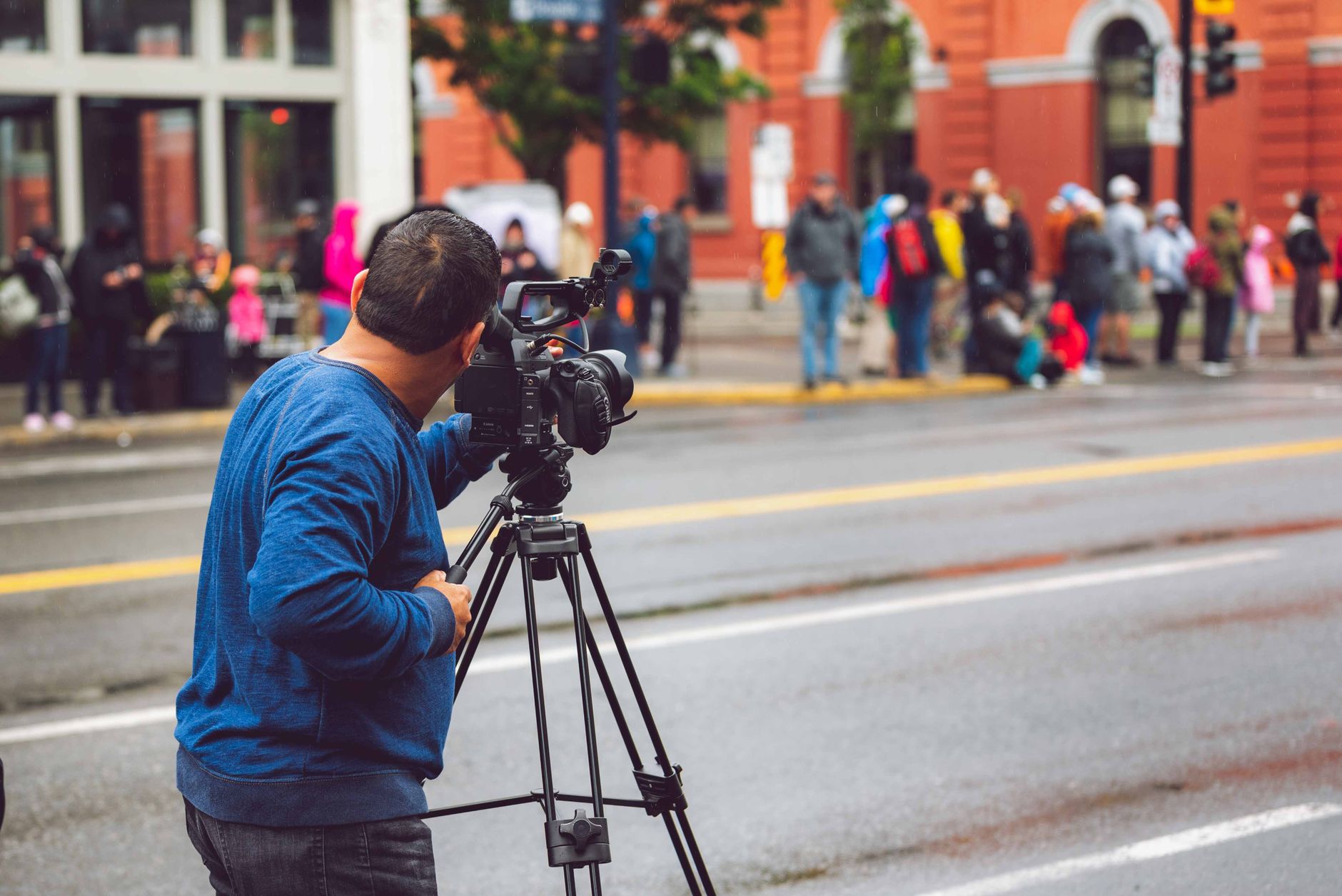 Filmare med videokamera på stativ vid en gata, förbipasserande på trottoaren i bakgrunden ur fokus