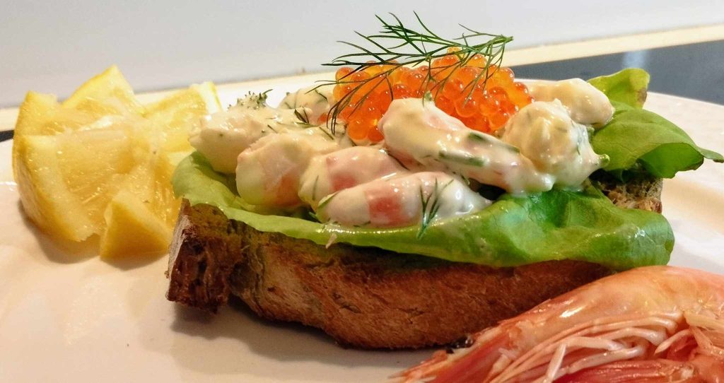 Toast Skagen med hela räkbitar i majonnäsröra, löjrom, salladsblad och citron på vit tallrik