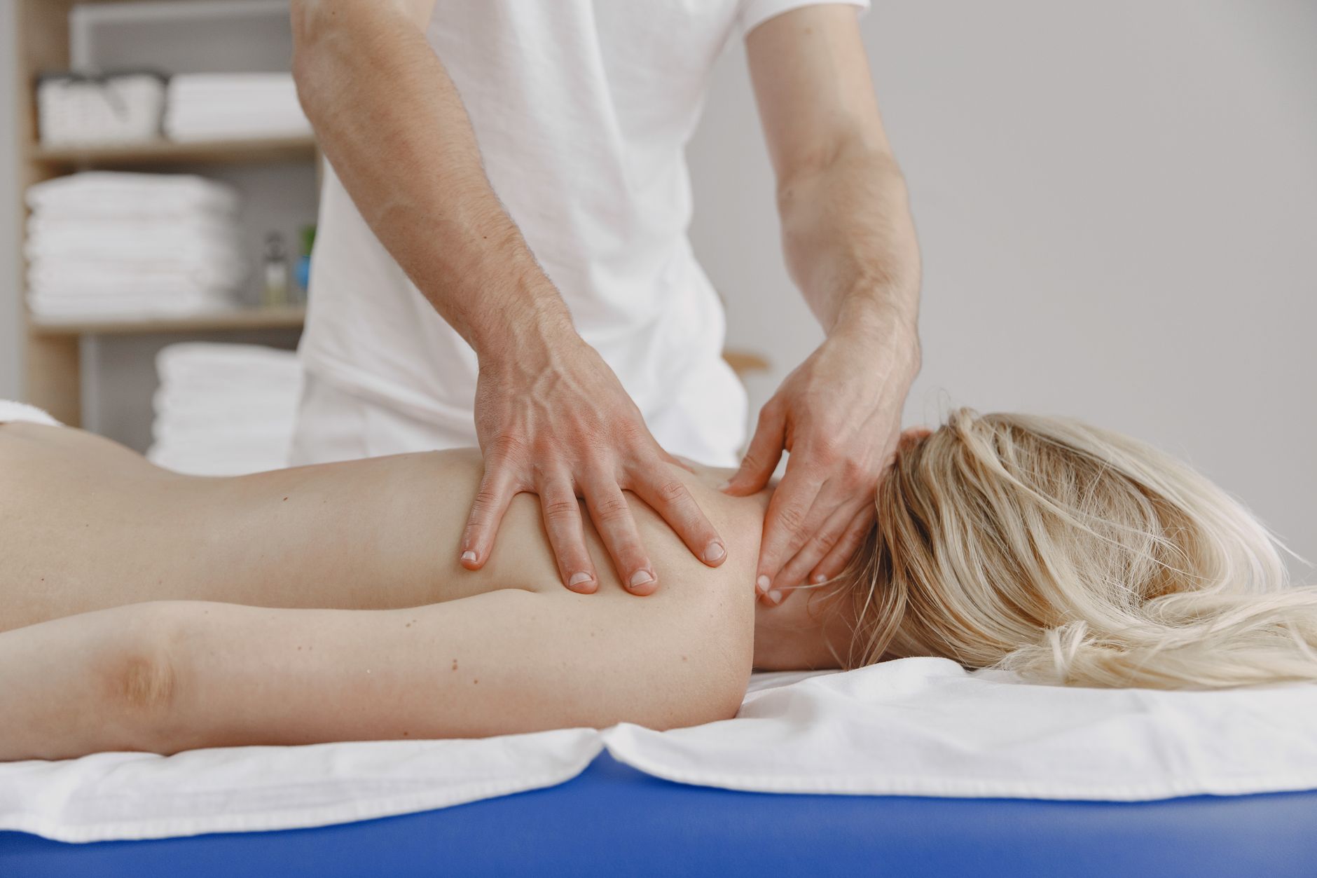 Massör som masserar nacke och skuldra på en kvinna på en massagebänk