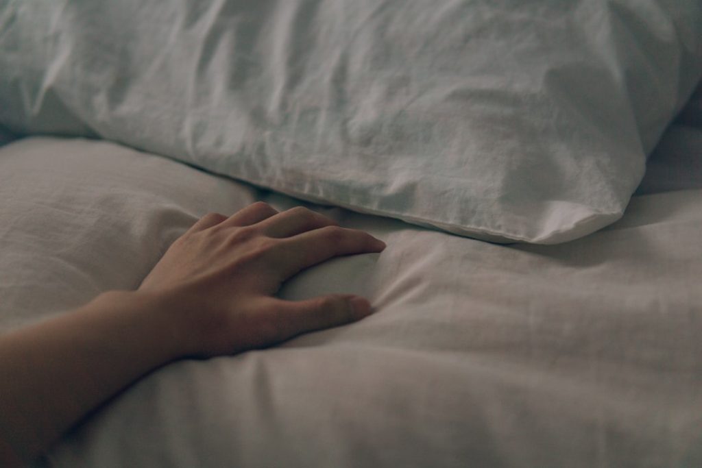 Hand som vilar vid kudden i en bäddad säng