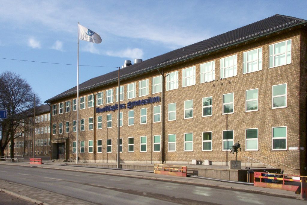 Thorildsplans gymnasiums gula tegelfasad med skolans namn i blå bokstäver, en marsdag med blå himmel.