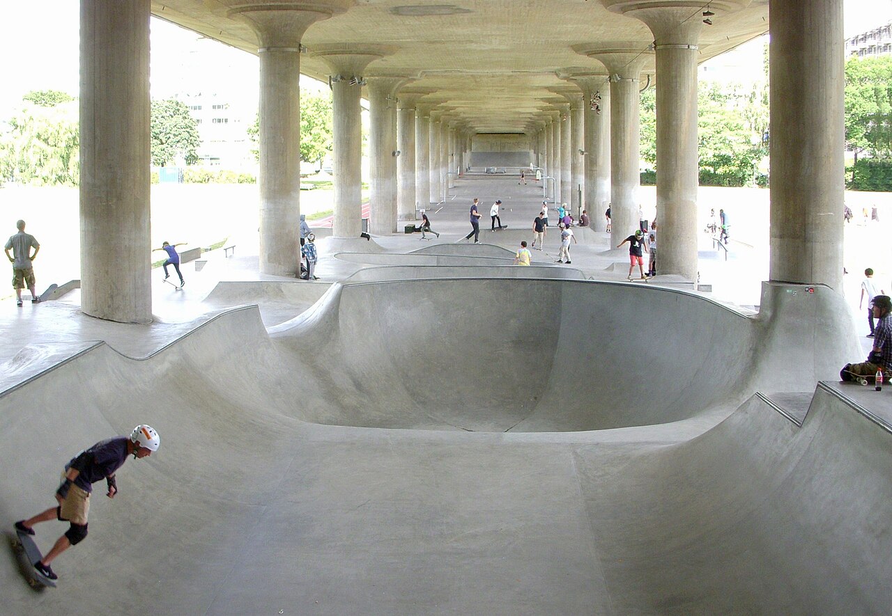 Skateparken under Lilla Västerbron i Rålambshovsparken, med betongbowl mellan brons pelare och åkare i bakgrunden.