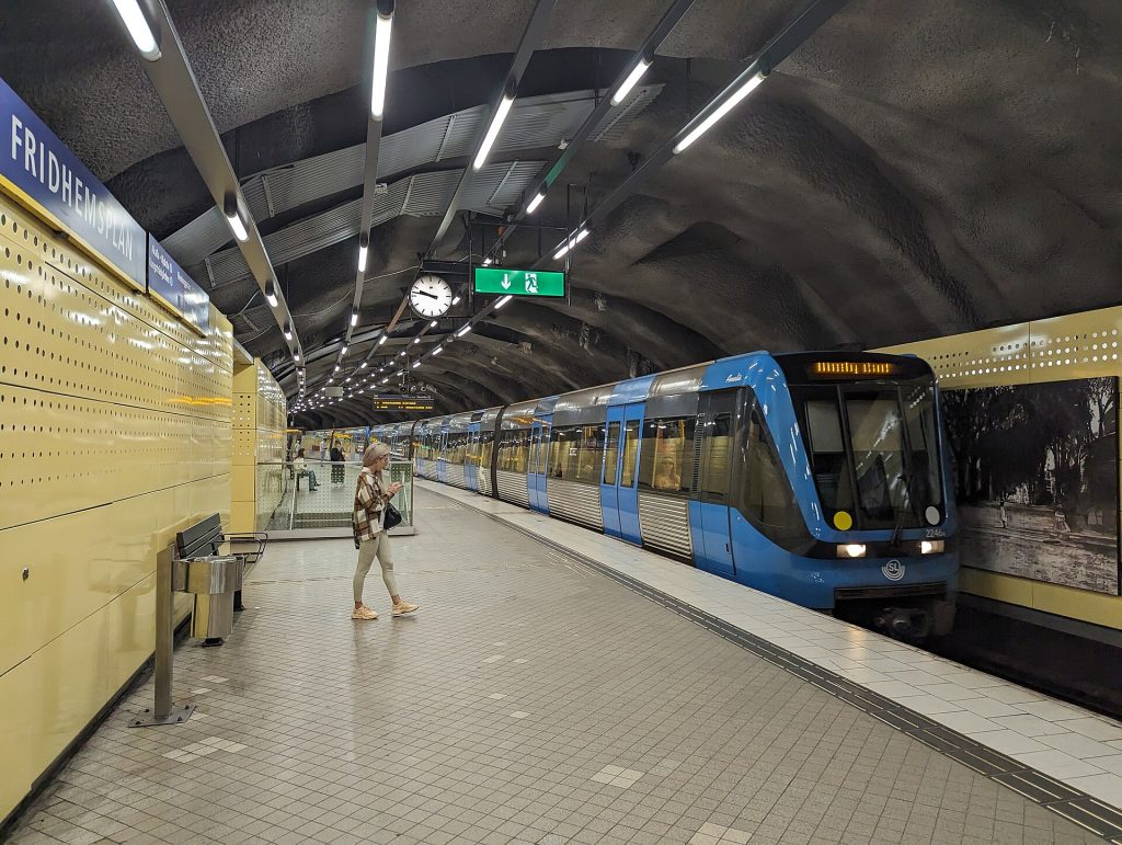 Gröna linjens perrong på Fridhemsplan med ett blått tunnelbanetåg vid plattformen och sprängt berg i taket