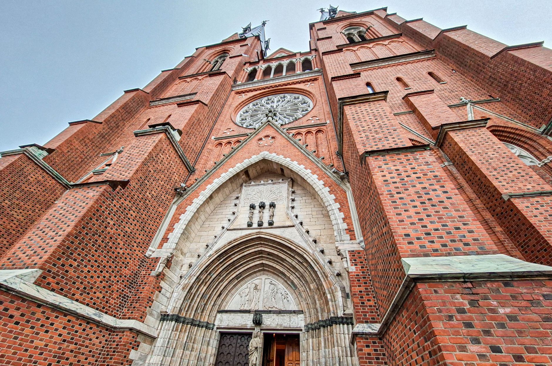 Uppsala domkyrkas västfasad i rött tegel med rosettfönster och den ljusa stenportalen, fotograferad underifrån