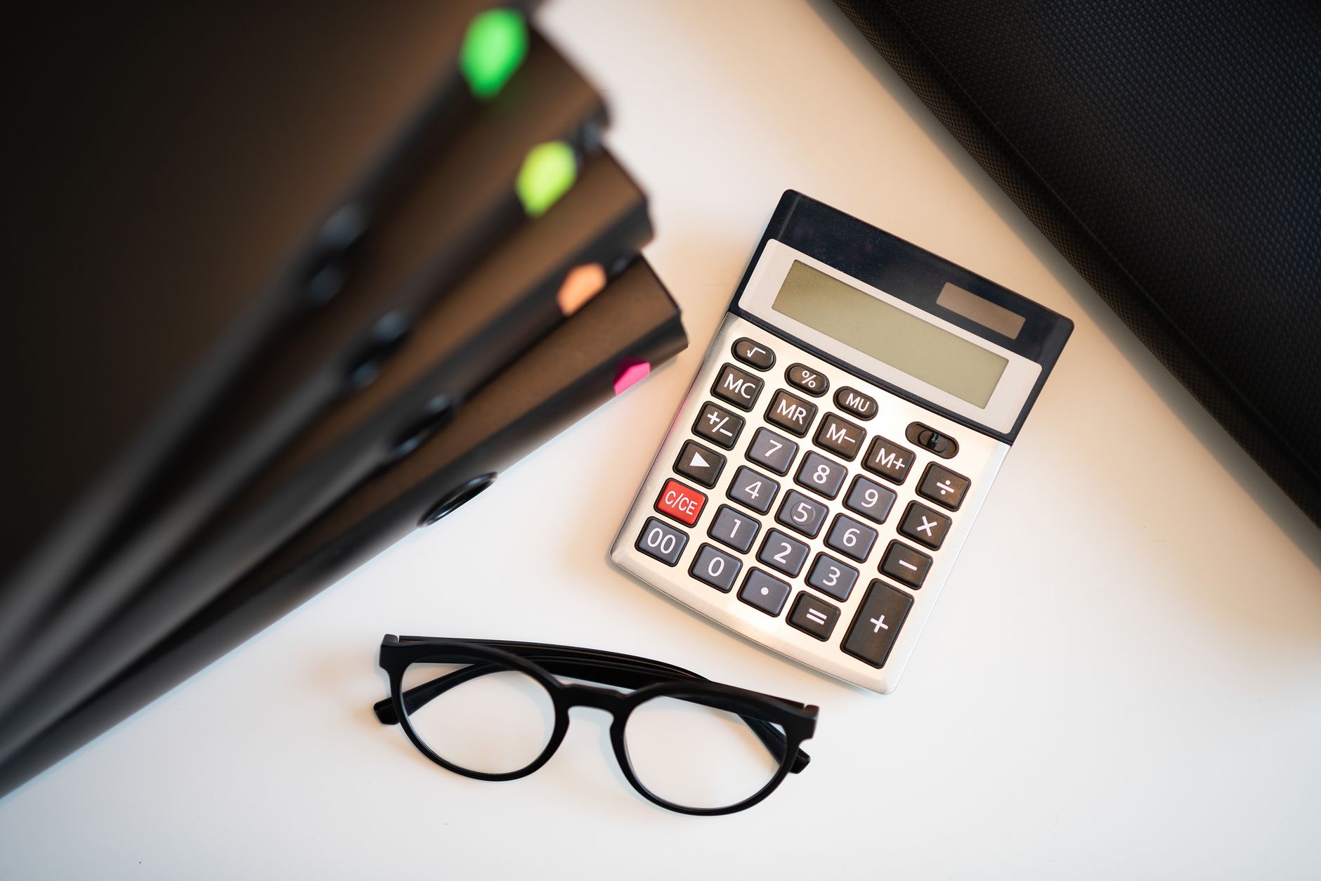 Calculator, glasses and ring binders on a white desk