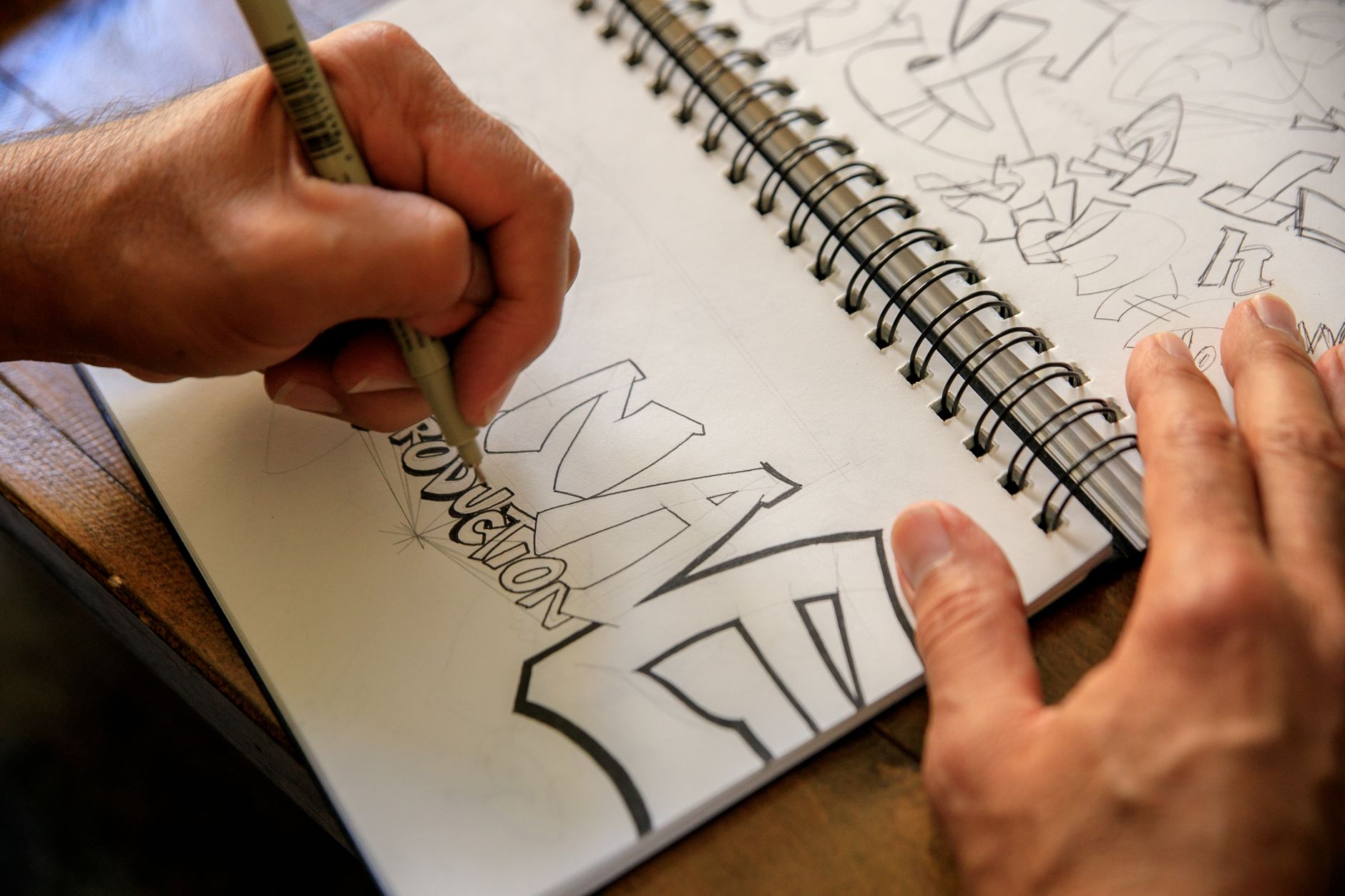 Hand som tecknar graffitibokstäver med fiberpenna i ett skissblock