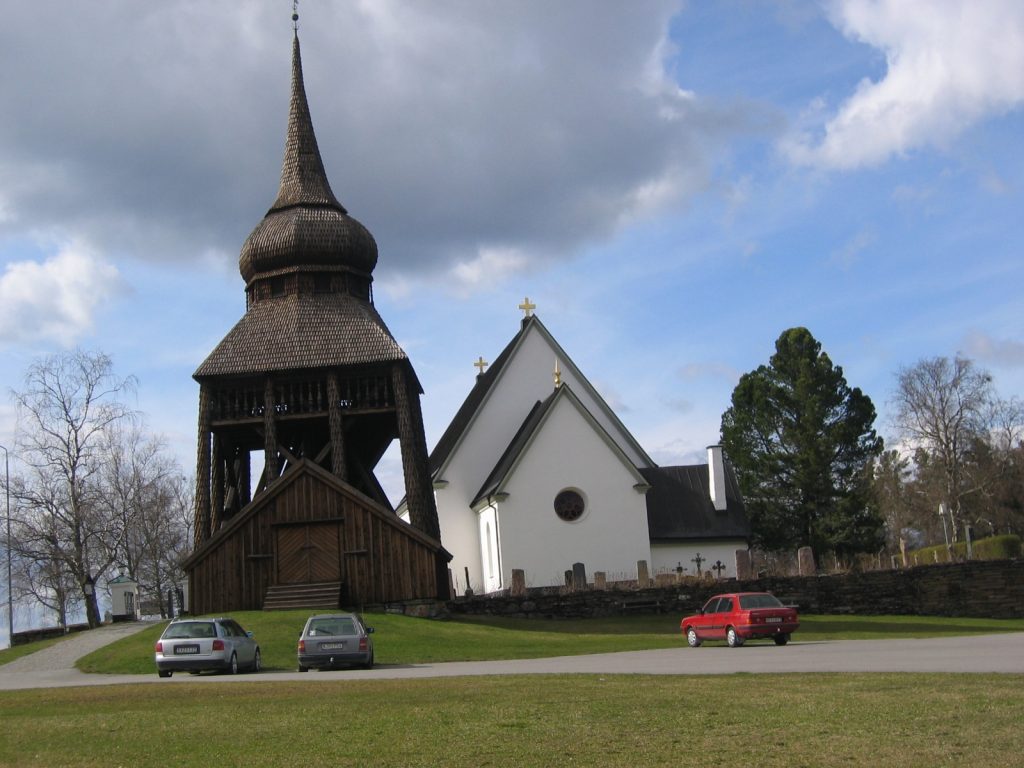 Frösö kyrka med vit fasad och den spånklädda klockstapeln med lökkupol framför