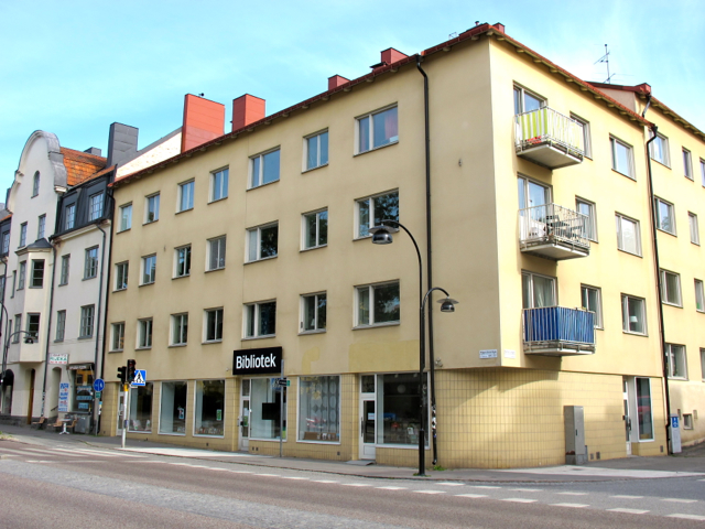 Gult hörnhus på Hägerstensvägen med skylten Bibliotek ovanför fönstren i bottenvåningen