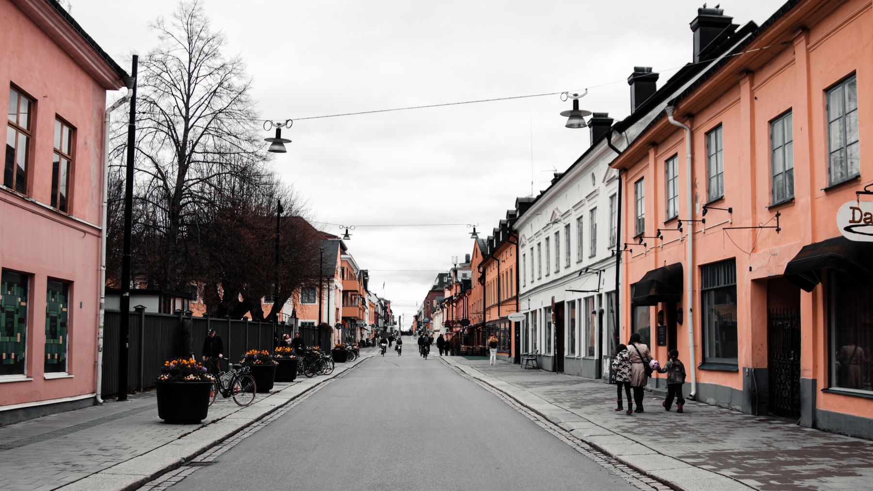 Gata i centrala Uppsala kantad av pastellfärgade trähus, med cyklar, planteringar och människor på trottoaren