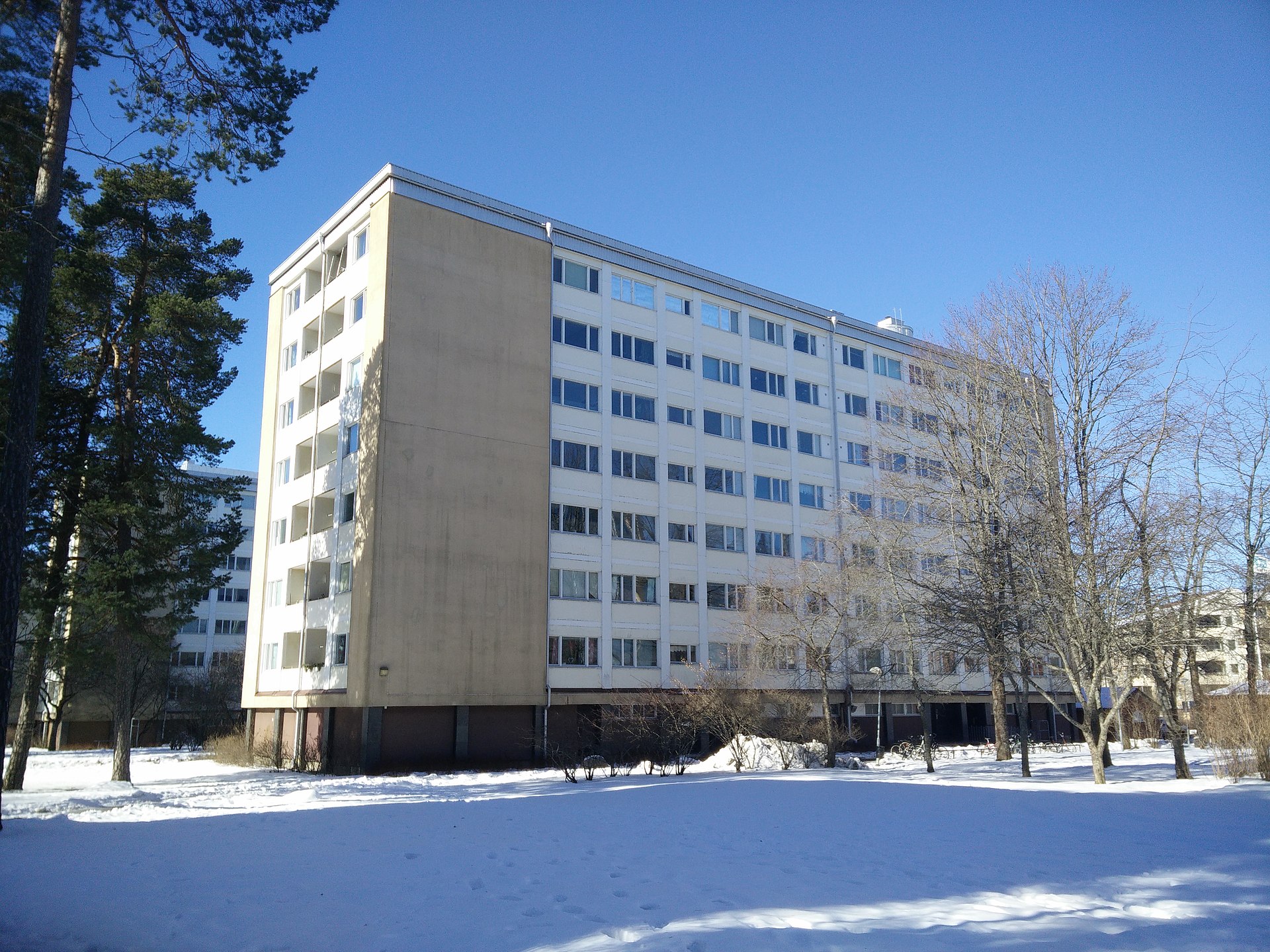 Ljust lamellhus i flera våningar omgivet av tallar och snö i stadsdelen Eriksberg i Uppsala