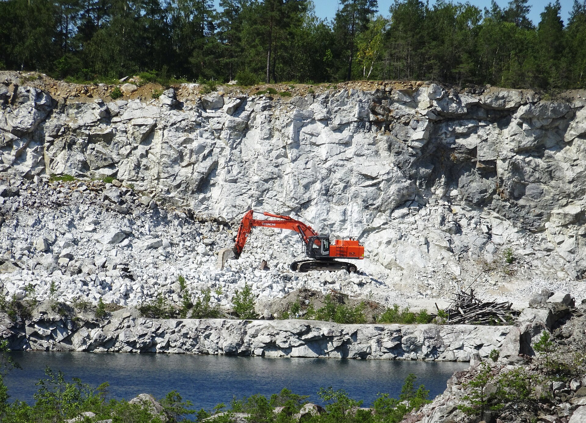 Vit kalkstensvägg i Stora Vika kalkbrott med en orange grävmaskin på pallen framför