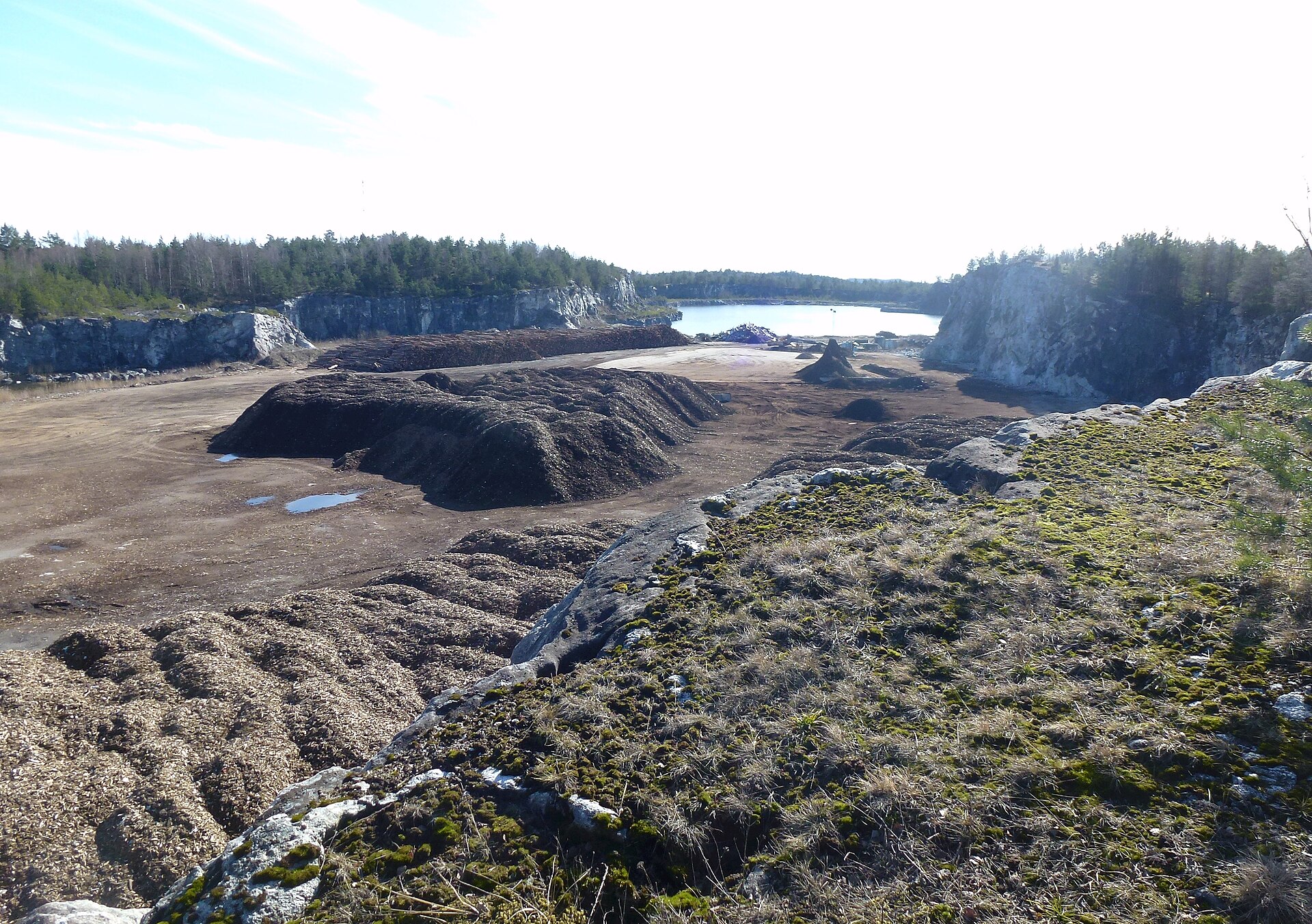 Norra brottytan i Stora Vika kalkbrott med stora högar av flis och bark, brottsjön i bakgrunden