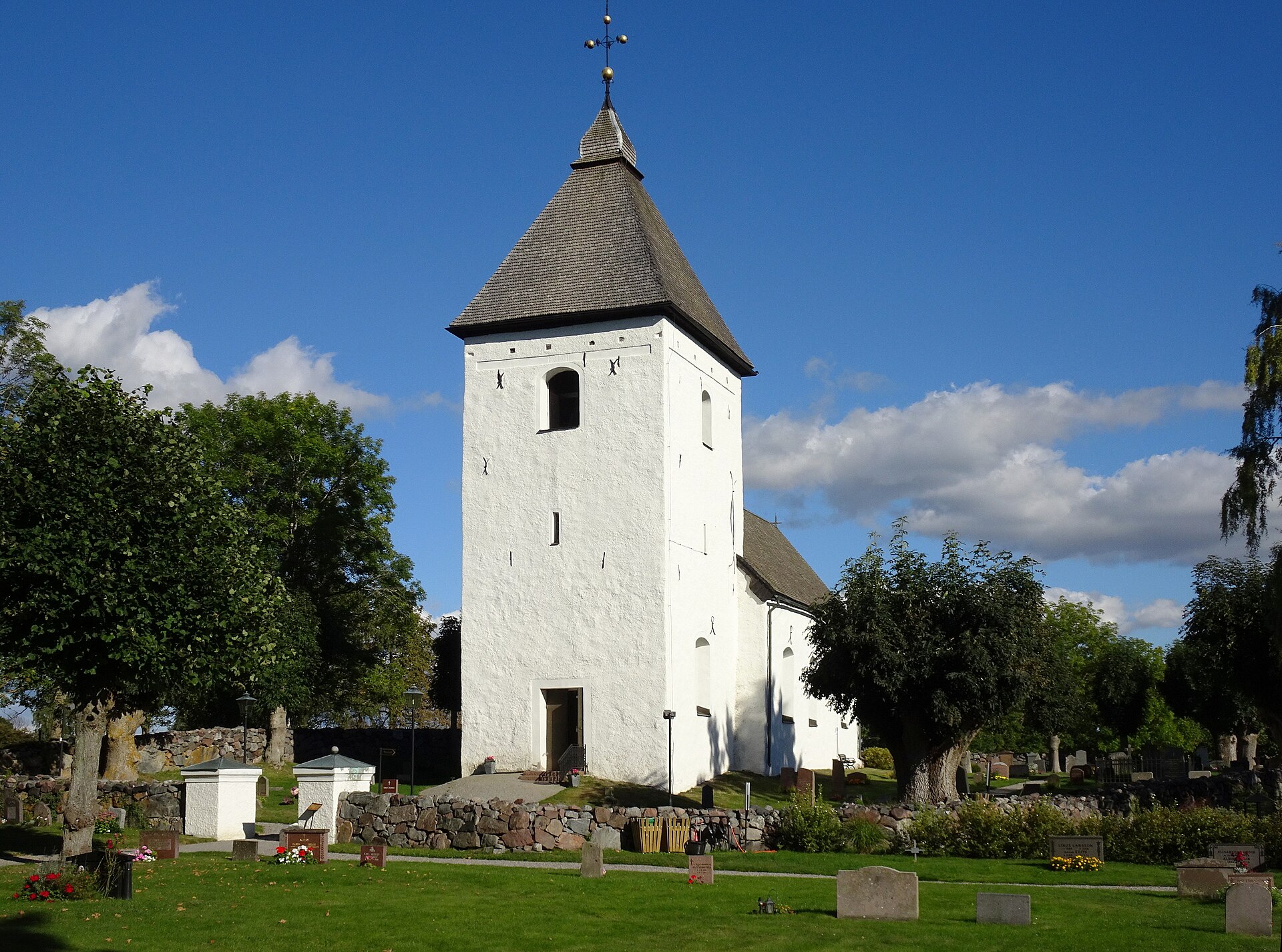 Adelsö kyrka med sitt vittputsade västtorn och spåntäckta tornhuv, sedd från kyrkogården