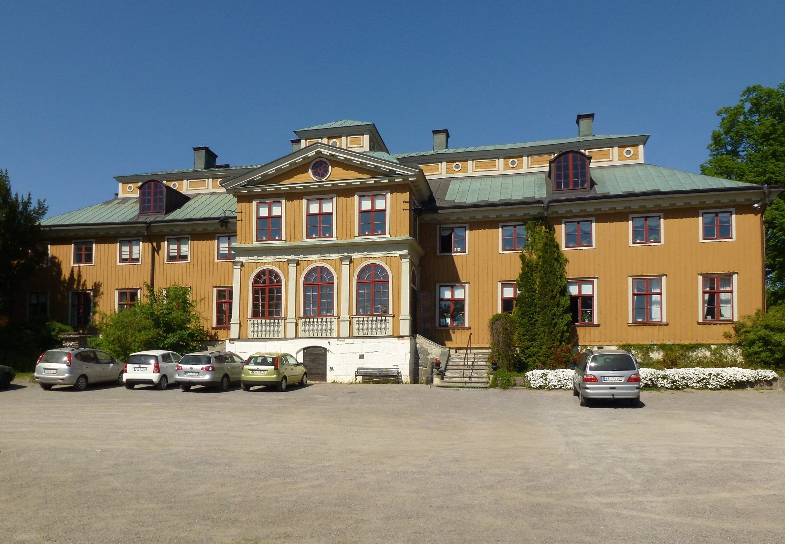 Ekebyhovs slotts gula träfasad med säteritak och balkong över entrén, sedd från uppfarten på södersidan
