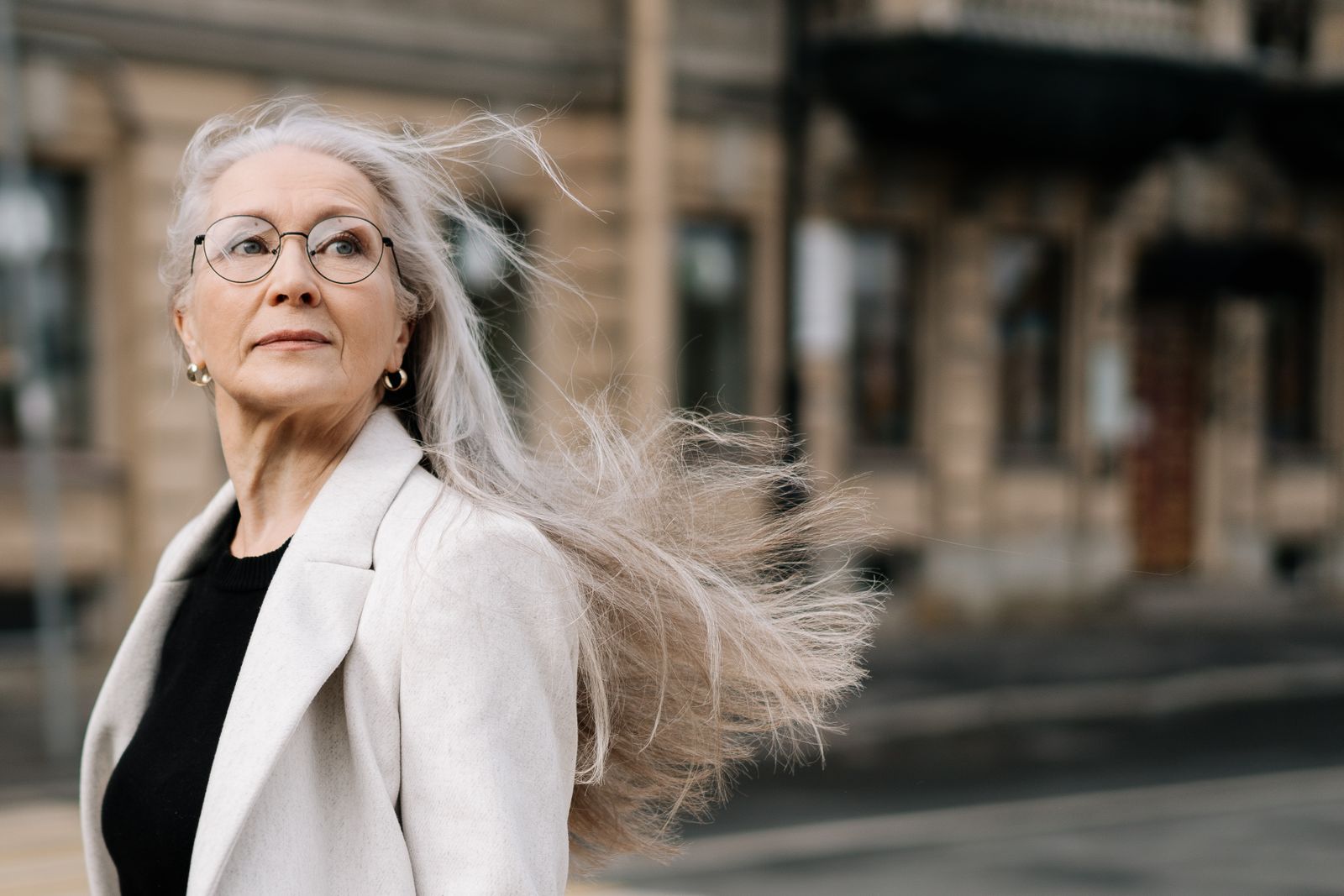 Kvinna med långt naturligt grått hår i blåsig stadsmiljö