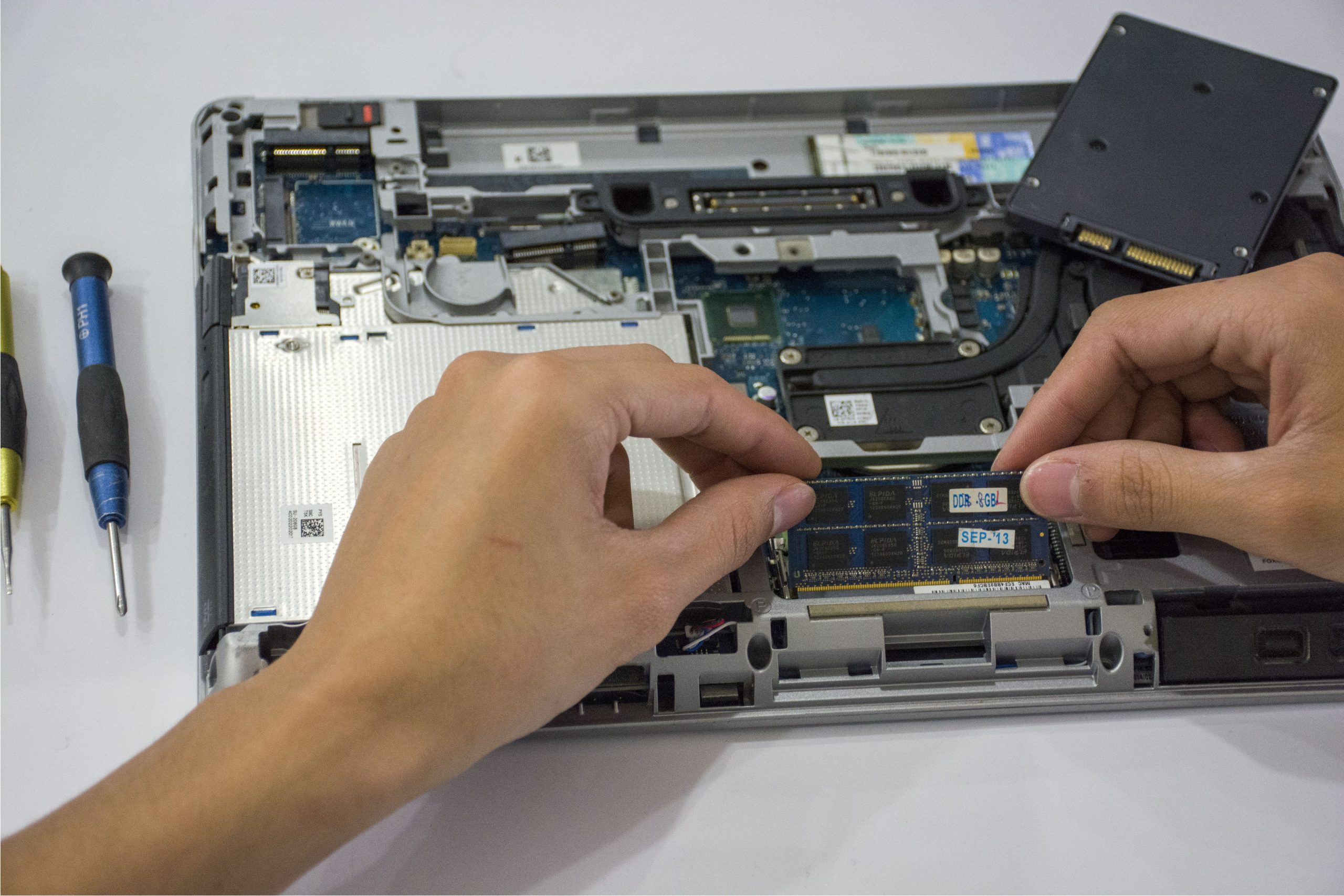 En tekniker sätter i en RAM-modul i en öppnad laptop, med en SSD synlig bredvid