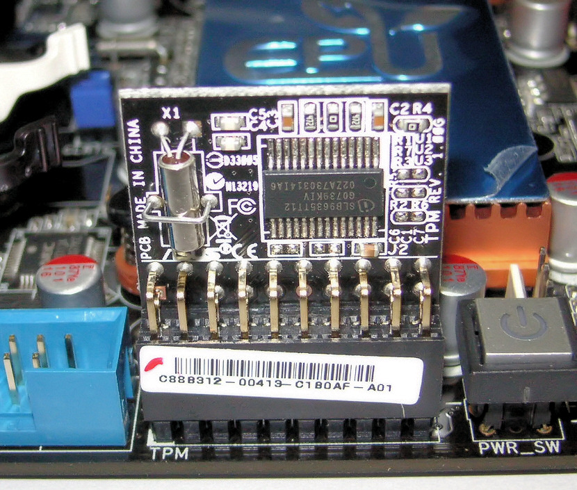 Ett litet kretskort med ett Infineon-chip sitter upprätt i en stiftlist på ett moderkort, där kortets eget tryck under listan säger TPM.