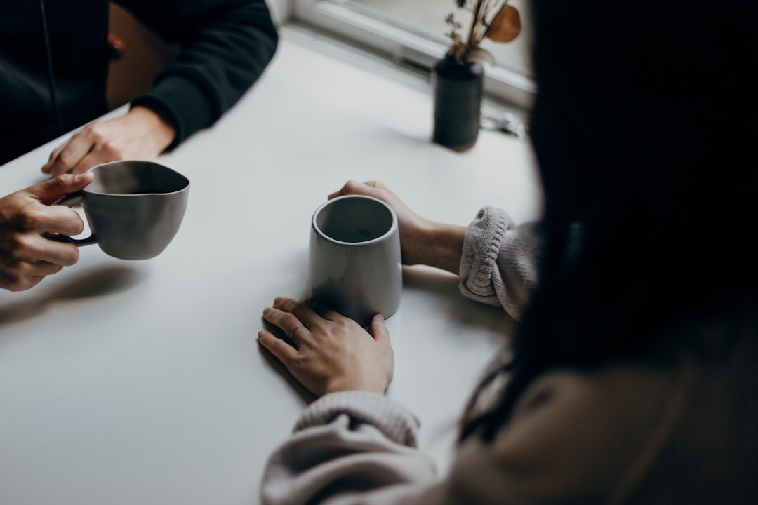 Två personer sitter mitt emot varandra med kaffekoppar vid ett bord