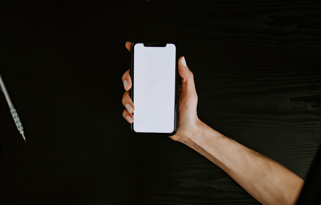 En hand håller en smartphone med tom skärm mot mörk bakgrund