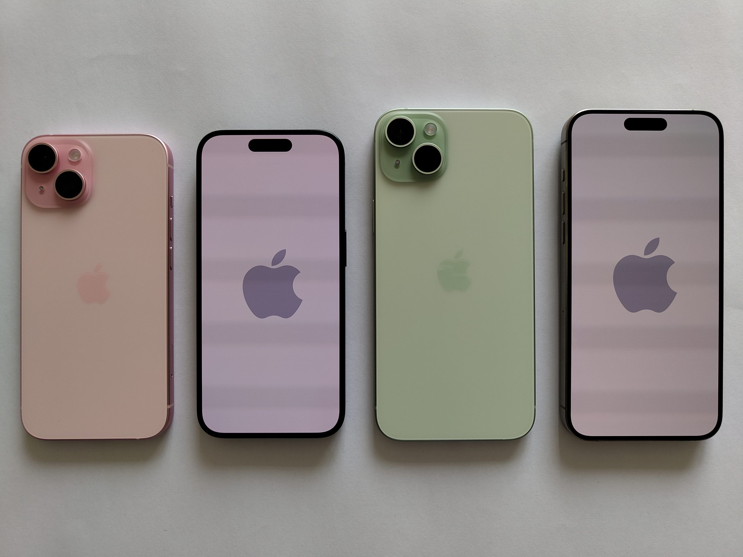 Fyra iPhone 15 i rosa och grönt, två med baksidan uppåt och två med skärmen uppåt, på vit bakgrund