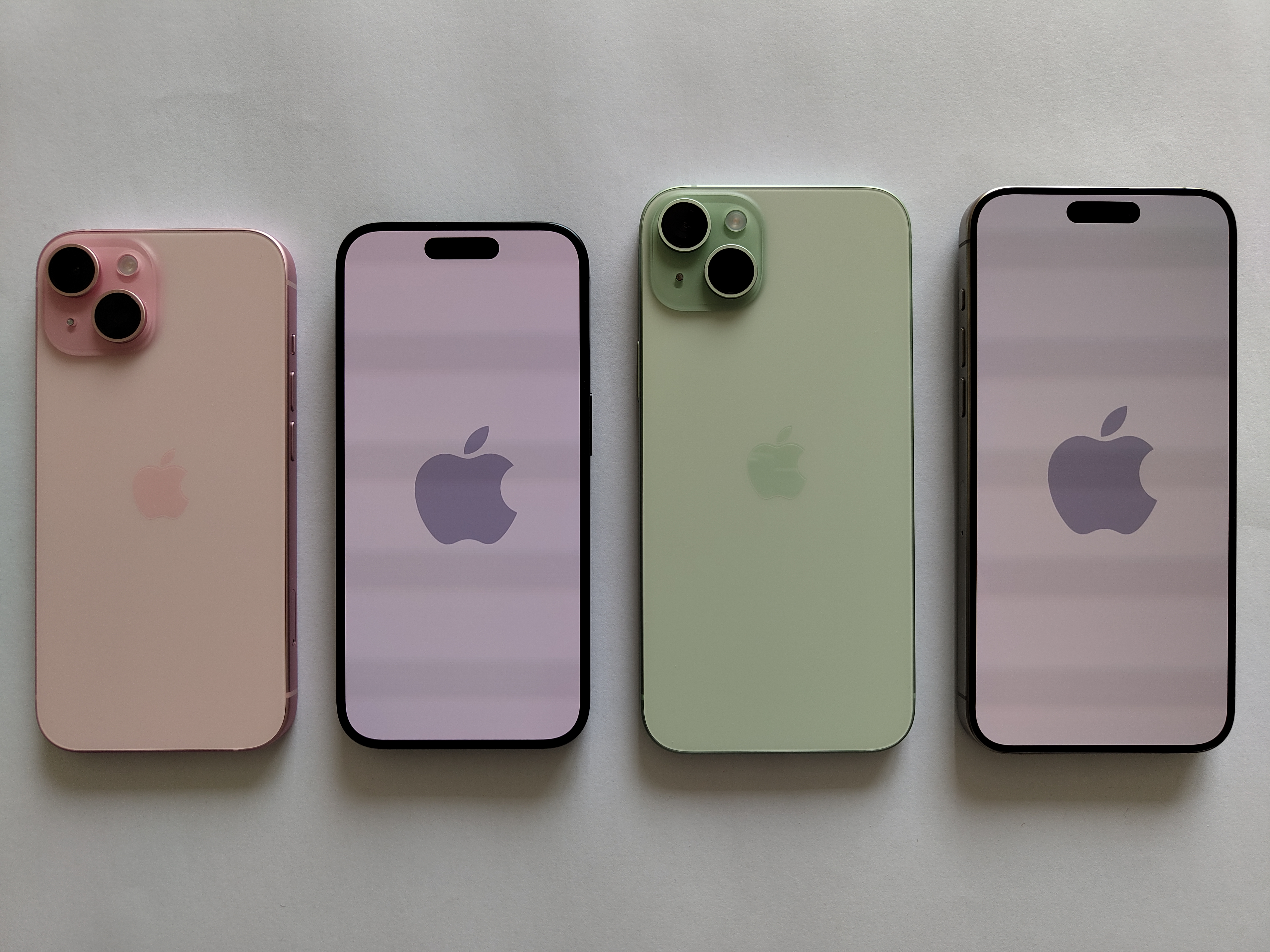 Fyra iPhone 15 i rosa och grönt, två med baksidan uppåt och två med skärmen uppåt, på vit bakgrund