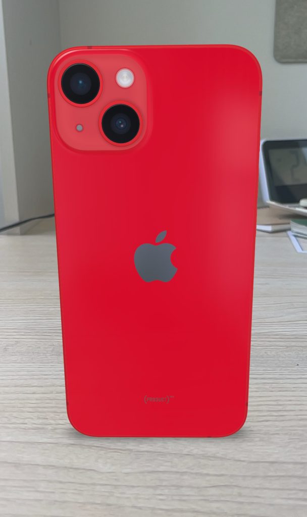 Röd iPhone 14 i (PRODUCT)RED ligger med baksidan uppåt på ett ljust skrivbord