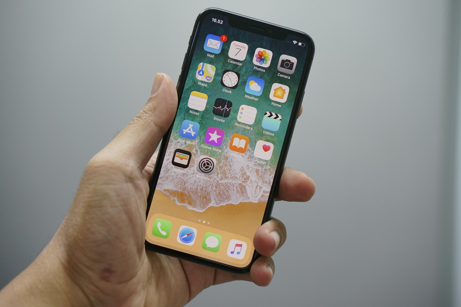 iPhone som hålls i handen och visar hemskärmen med bakgrundsbild och appsymboler