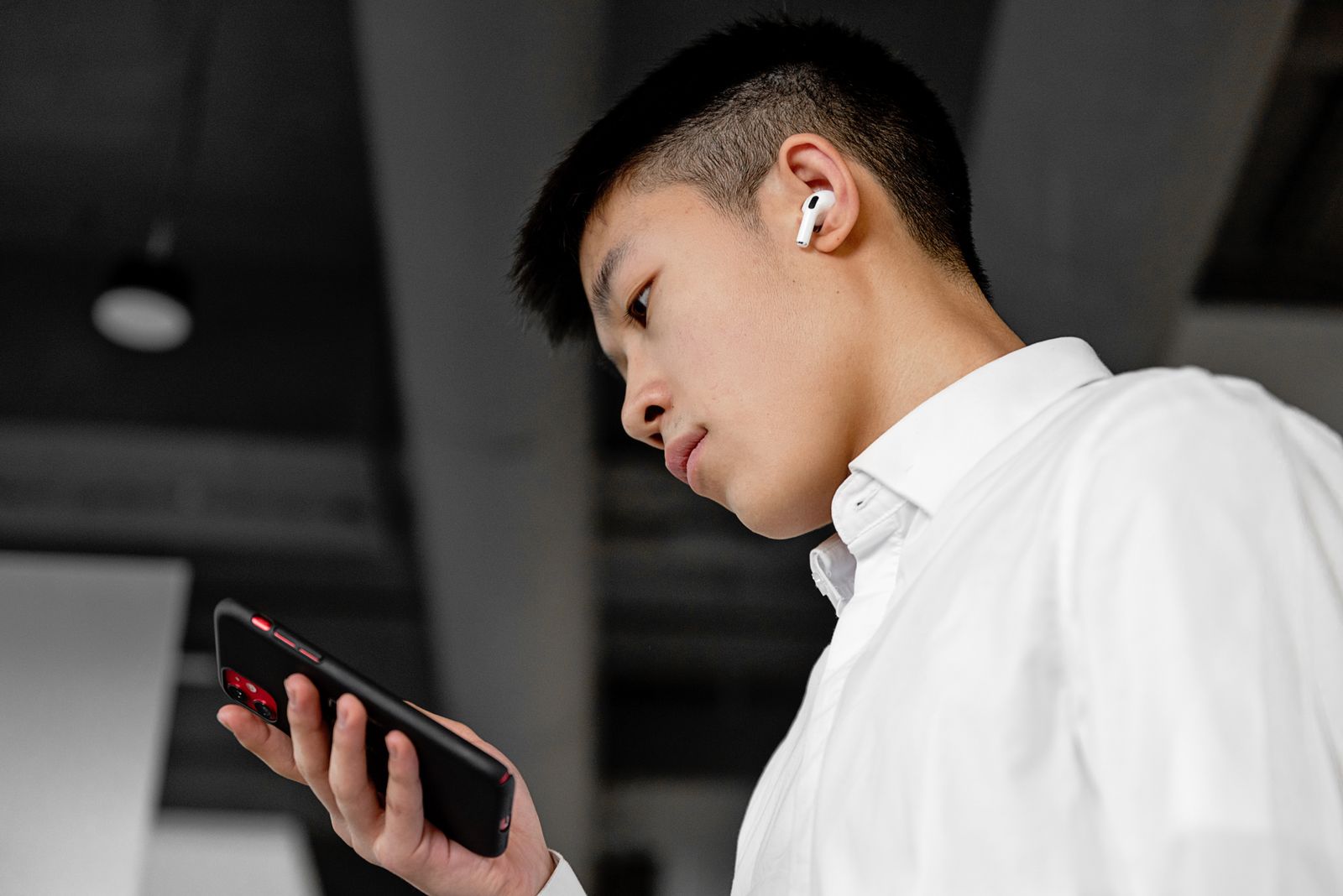 Ung man med vita AirPods i örat tittar på sin iPhone