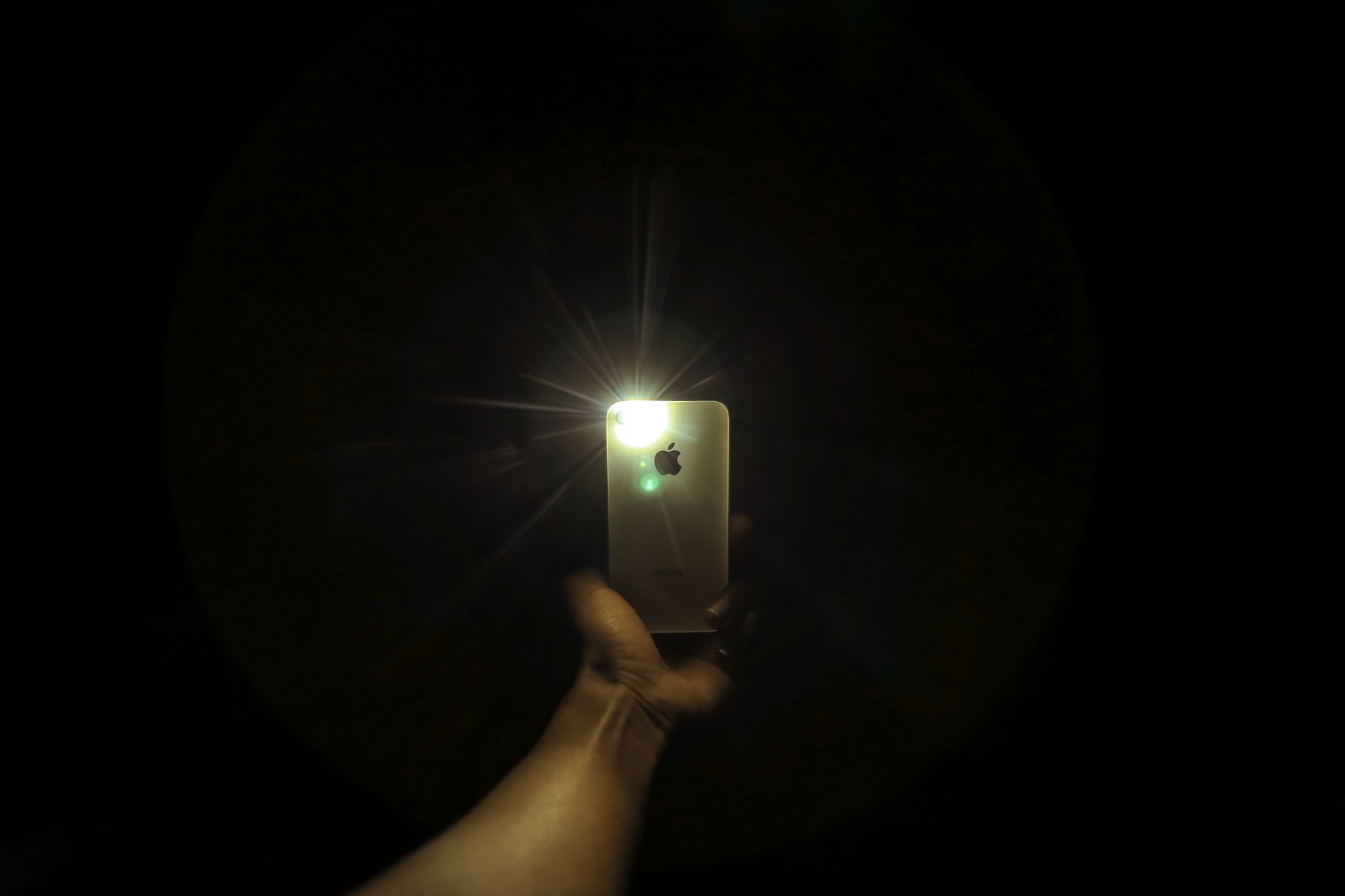Hand som håller en Iphone med tänd ficklampa i mörker