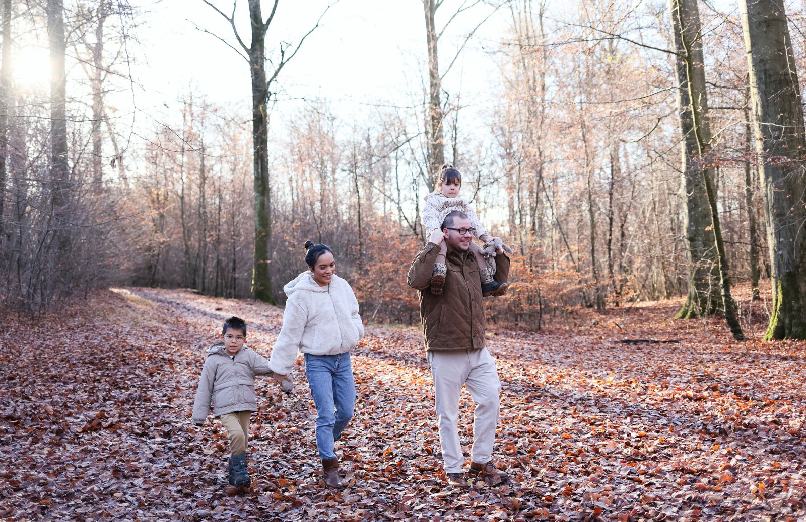 Familj med två barn på promenad längs en lövtäckt stig i höstskog