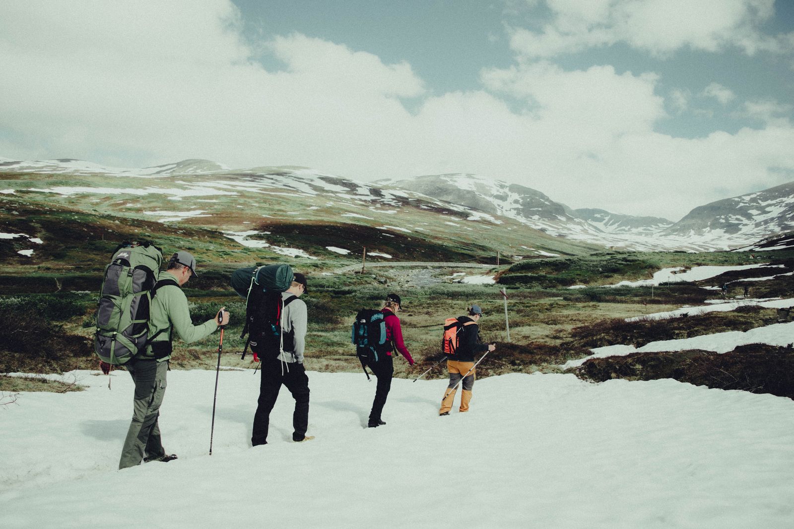 Vandrare med stora ryggsäckar på en led i ett snöfläckigt fjällandskap