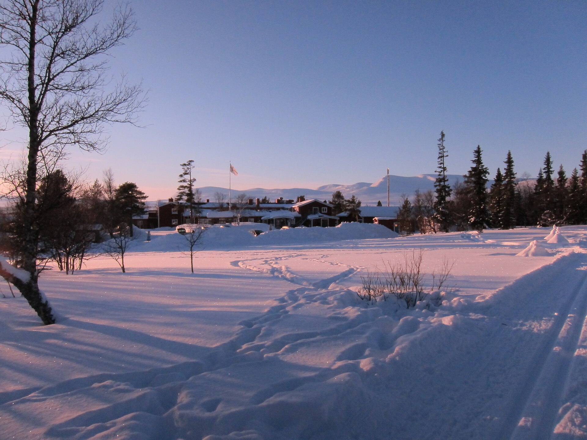 STF Grövelsjön Fjällstation i skymningsljus en vinterdag, med snötäckt mark och fjäll i bakgrunden